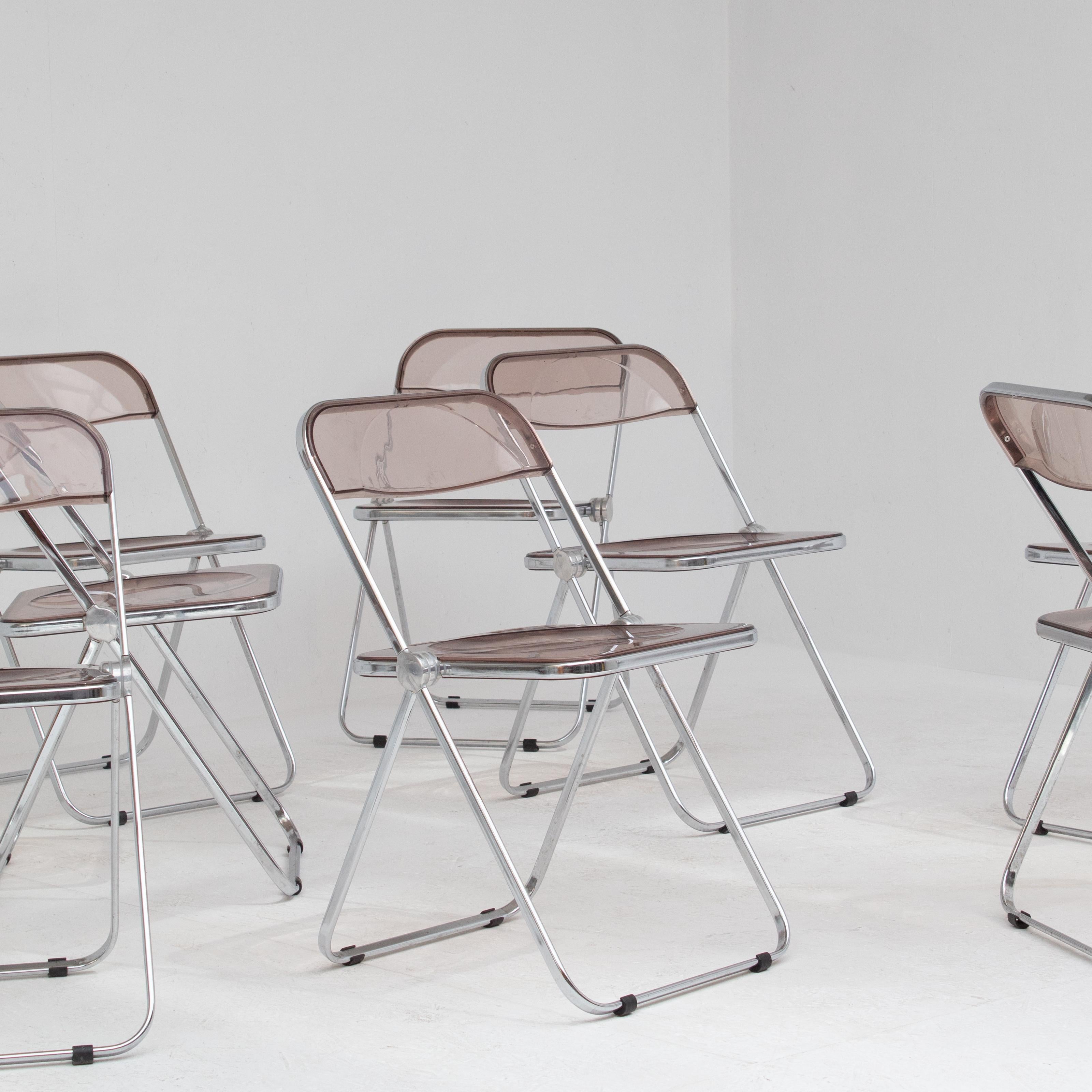 Este original conjunto de sillas Plia de Giancarlo Piretti consta de ocho sillas plegables con estructura cromada y asiento y respaldo de acrílico ahumado. Diseñada en 1967 para Castelli, la silla Plia se convirtió rápidamente en un icono del diseño