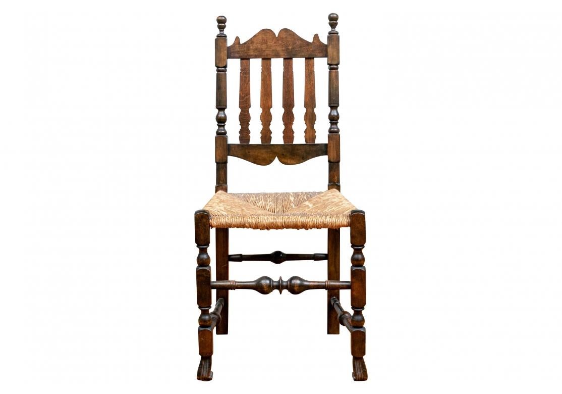 Rustic set of eight English Country style banister back chairs in dark stained maple with tightly woven rush seats.

Each Chair measures 17.5” wide by 15.25” deep by 39.5” high. Seat height 18.5”. 

Condition: In overall distressed condition and 