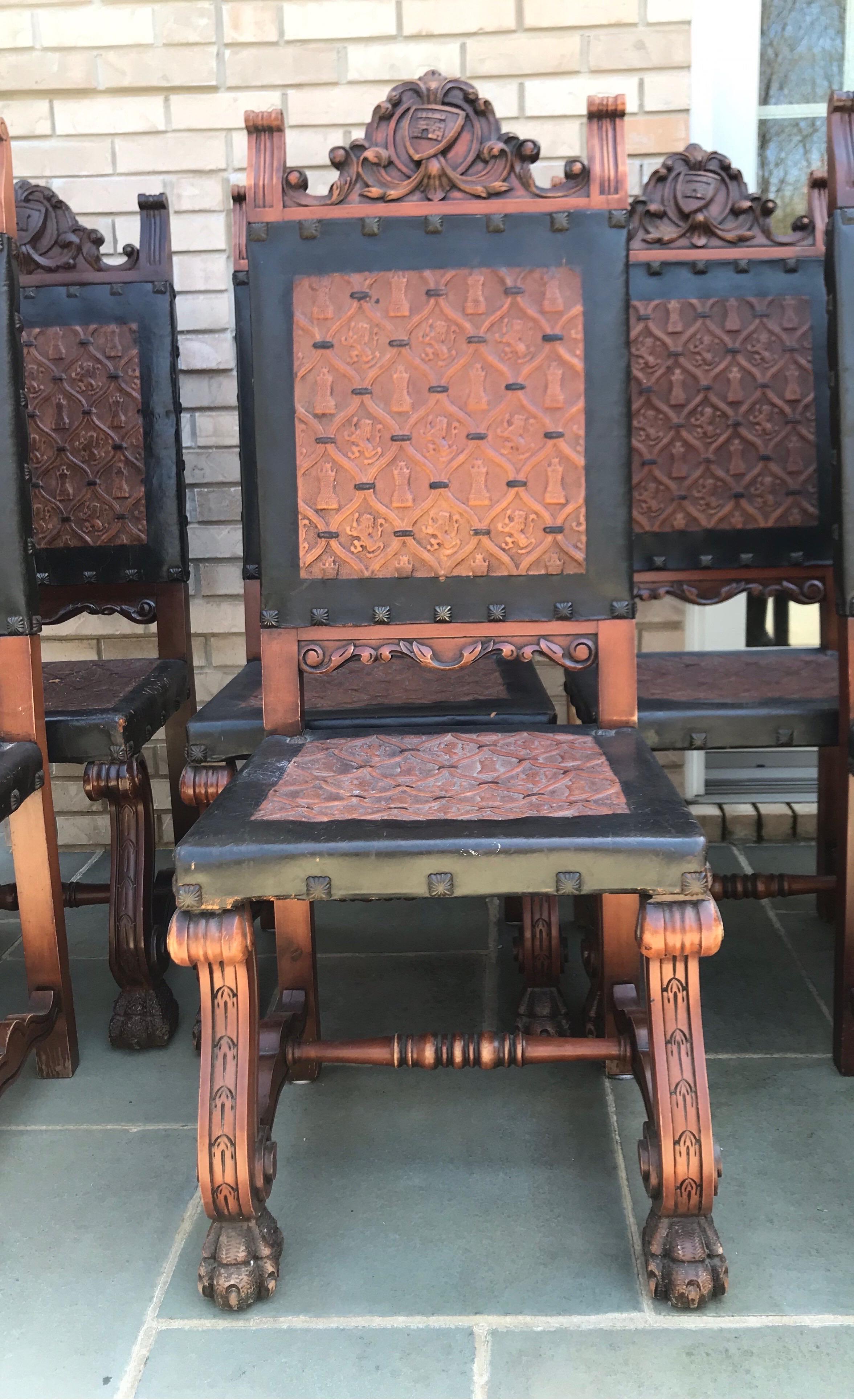 Set of 8 antique Renaissance-style dining chairs. These chairs are sturdy and feature lion’s feet, a crested shield at the top, and very unique embossed leather. The leather has medieval towers and lions. Large metal tacks finish off the details.
