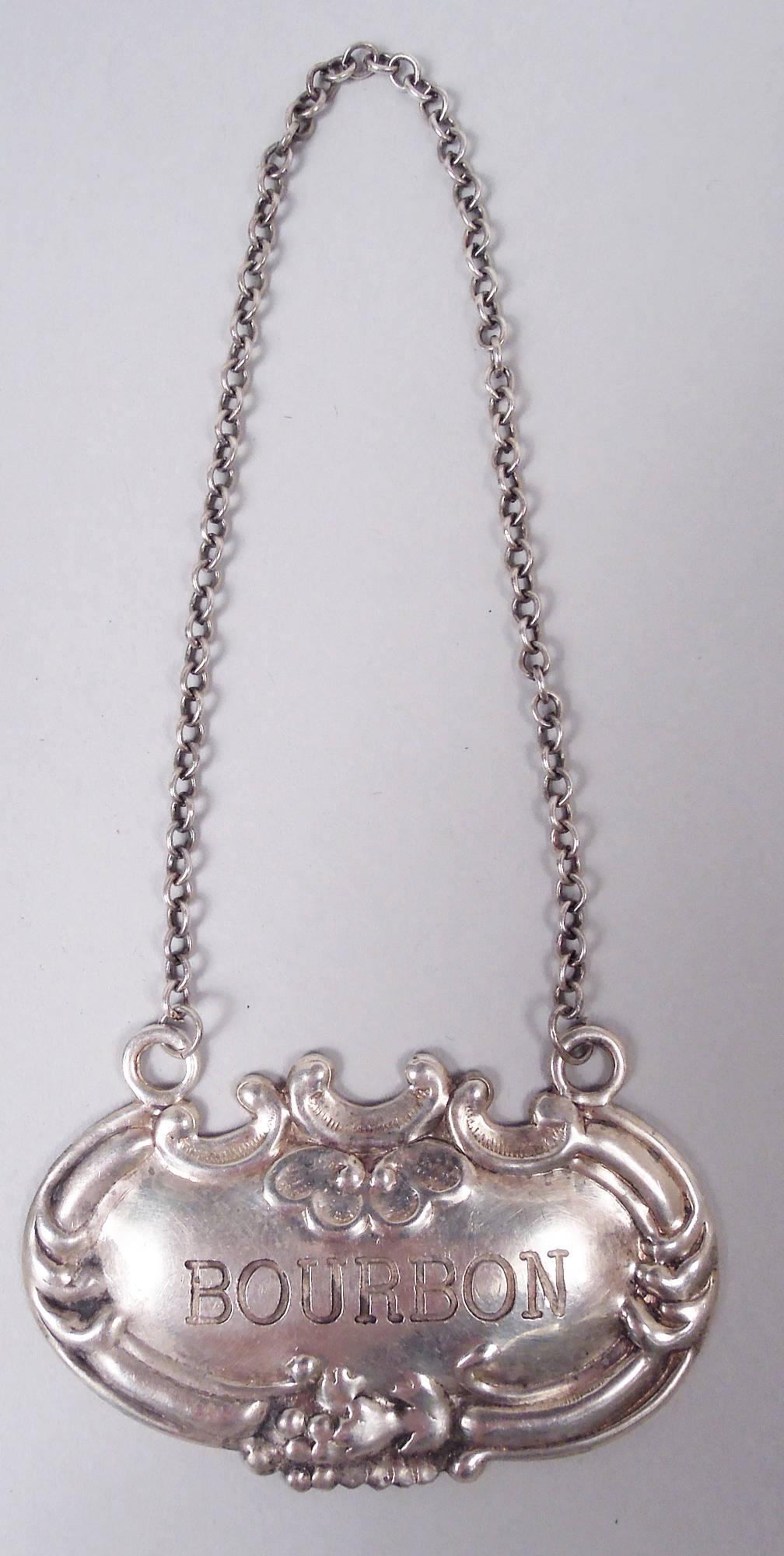 Set di 8 etichette tradizionali americane in argento sterling, 1910 circa. Ognuno: ovale orizzontale con cartiglio e fiore in rilievo; catena. Tipo di bevanda incisa: bourbon (2), sherry (2), scotch (1), gin (1), porto (1) e vodka (1). Timbro del