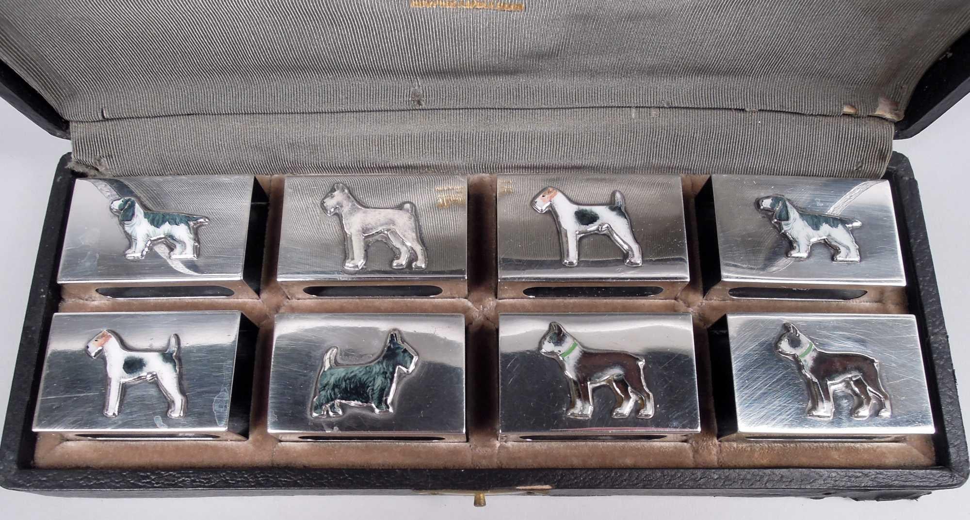 Set of 8 American Modern sterling silver matchbox holders, ca 1920. Retailed by Udall & Ballou in New York. Rectangular with open ends; sides have cutout tubes. On each is applied enameled dog. Five breeds represented. On back engraved block