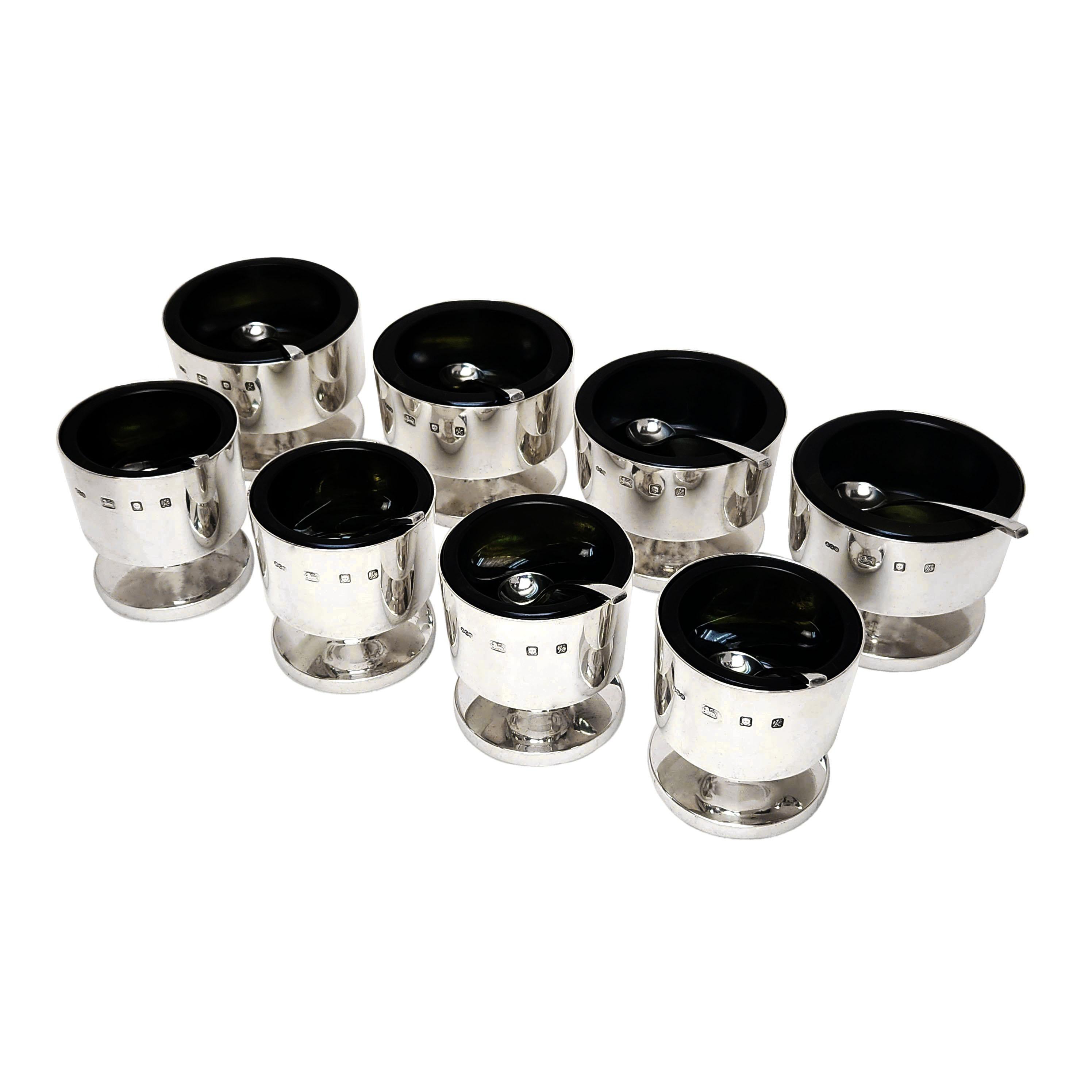 A magnificent suite of 8 Modernist Condiment Dishes by Gerald Benney. The Set comprised of 4 Mustard Pots and 4 Salts, each with a matching Benney spoon. The Condiment Pots have plain polished cylindrical forms on a spread foot. Each Dish has a