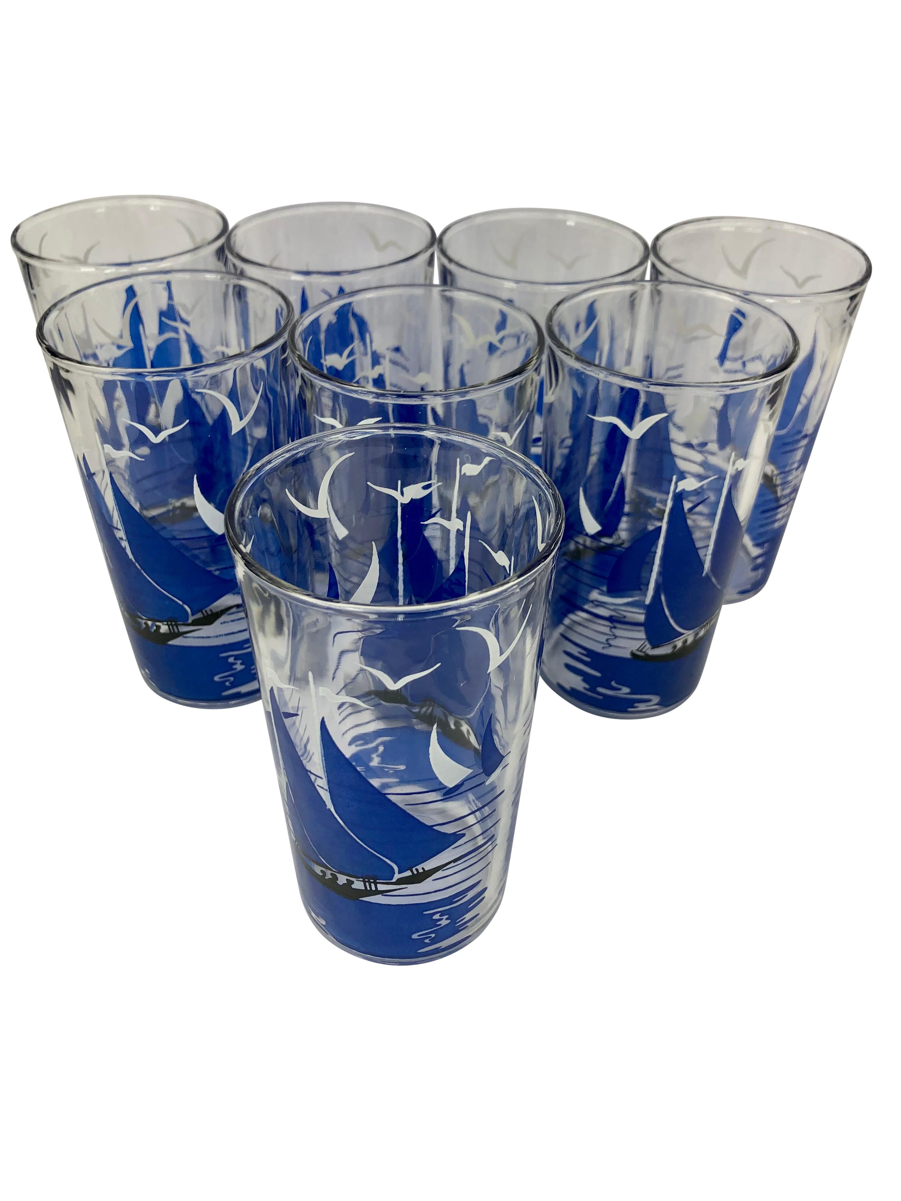 Set of 8 Vintage Tumblers in a Boat-Shaped Caddy. Glasses are decorated with blue sailboats in the ocean and white birds in the sky. Glasses measure 4 3/4