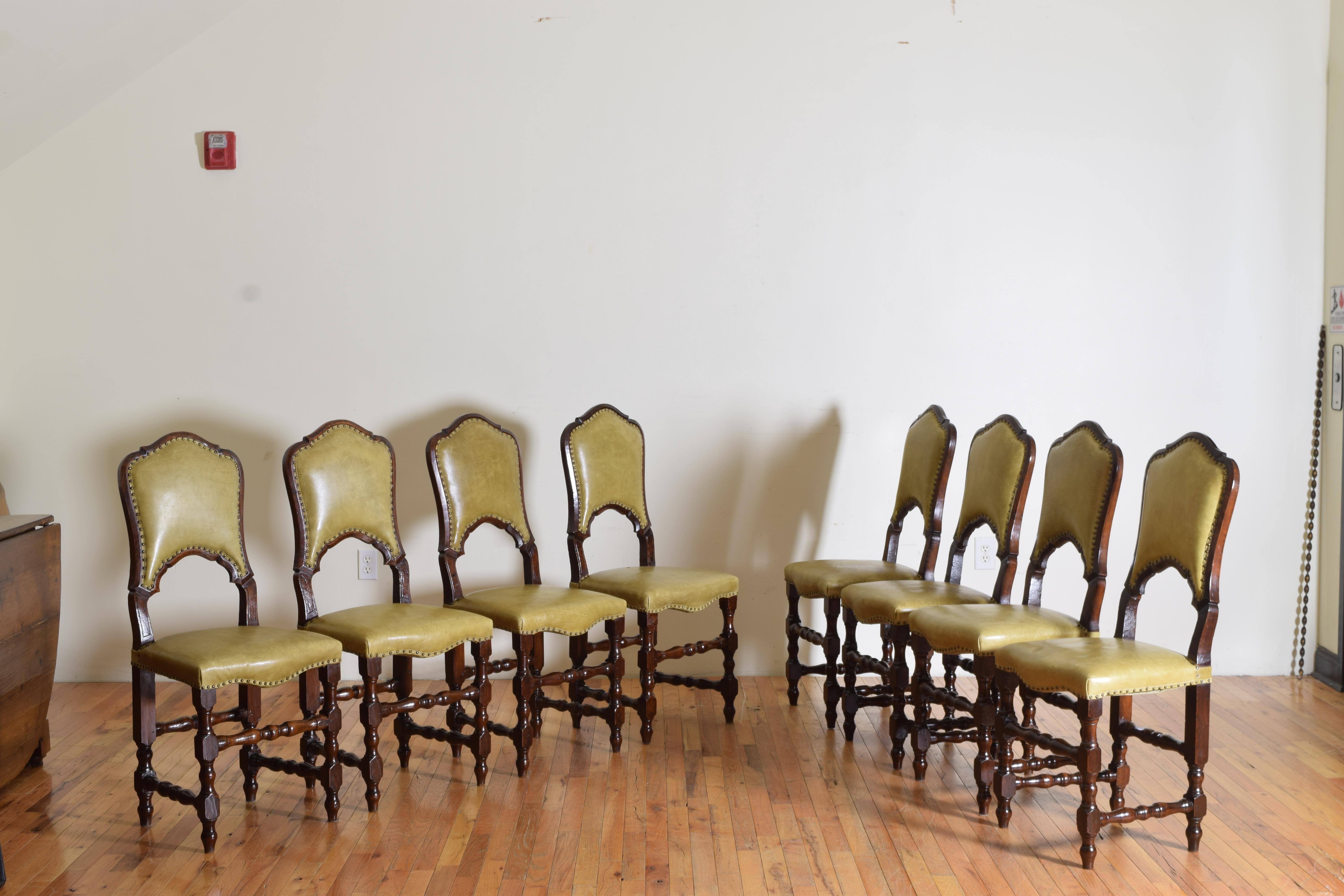 An interesting set of eight leather and walnut dining chairs with carved backs and turned legs ending on tapered feet.