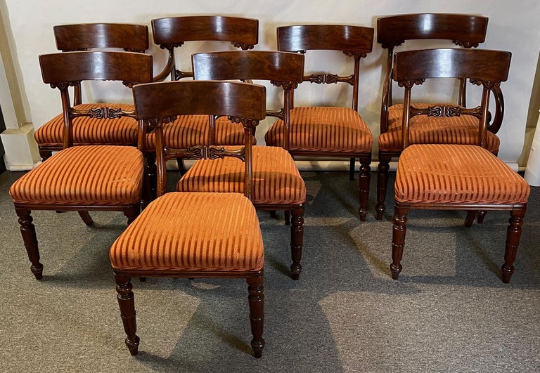 A set of eight early 19th C. English William IV mahogany dining chairs comprising two arms and six sides with persimmon colored upholstered seats. The chairs are substantial in size for the period and very sturdy with a large top rail, nicely carved