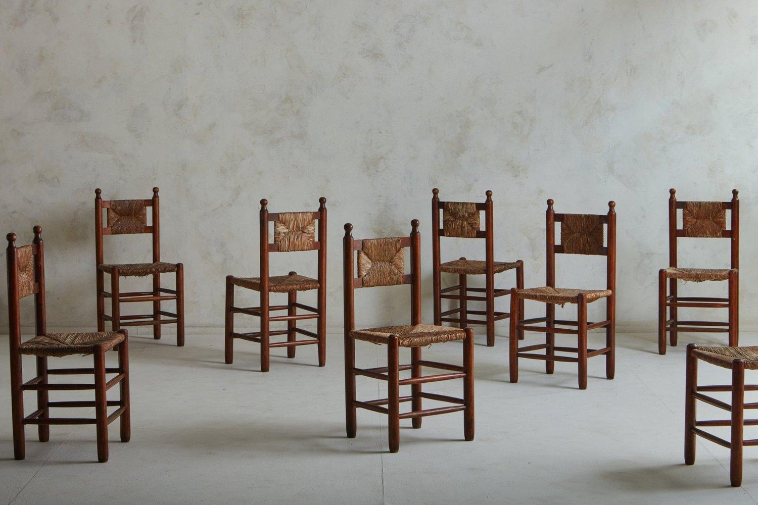 A set of 8 French 1940s dining chairs in the style of Charles Dudouyt. These chairs feature stained wood frames with circular finials and double stretcher details. They have woven rush seats and backs. Unmarked. Sourced in France, 1940s.