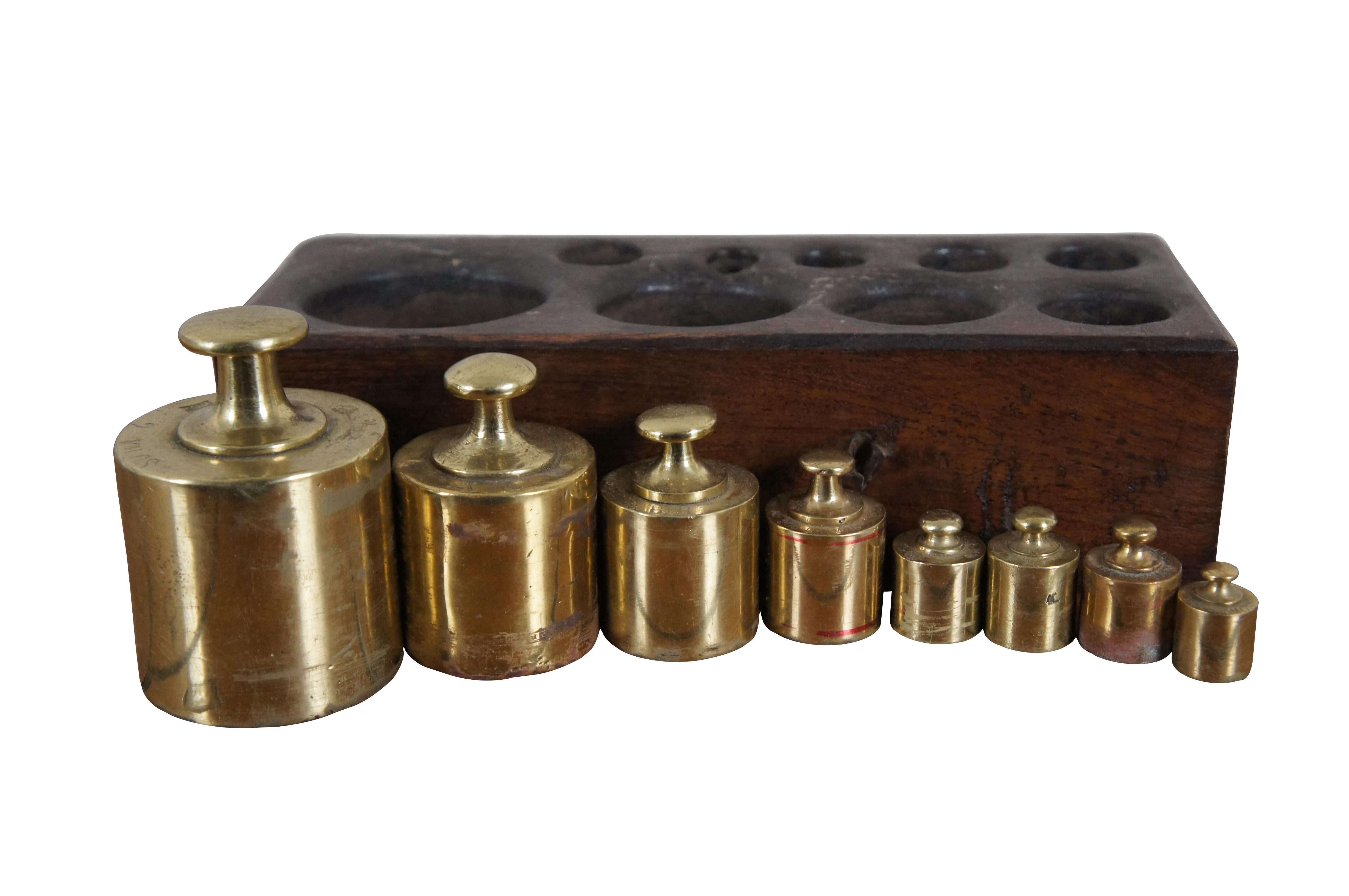 1920's brass apothecary scale weight set including nine weights (one 50 gram, three 100 grams, one 200 grams, one 500 grams, one 1 kilo, and one 2 kilos) set in a wooden block. Block contains an empty slot for what would presumably be a 25 gram
