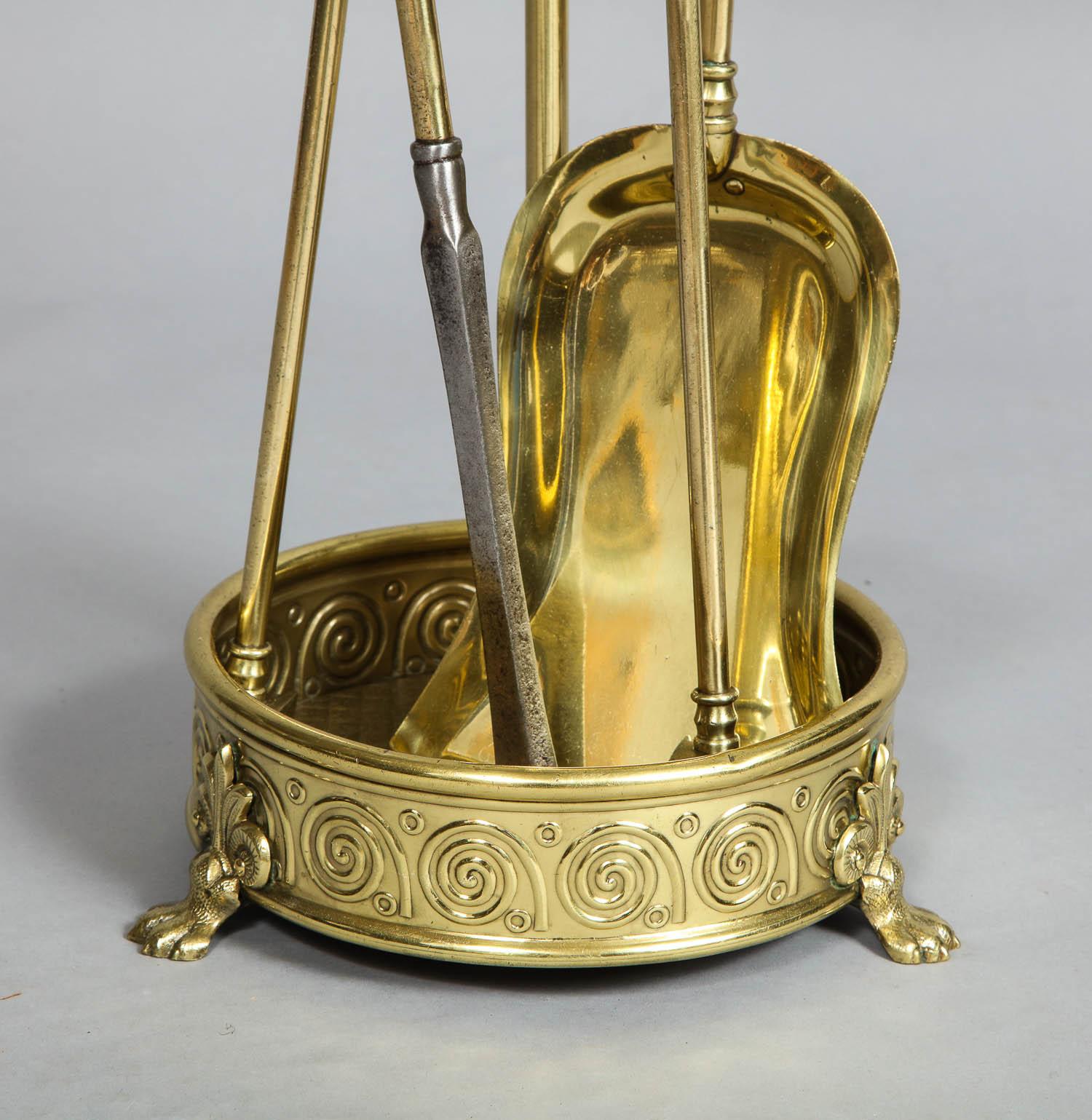 Good set of late 19th century aesthetic movement brass fire tools and matching stand, comprising a poker, tongs, and shovel all with ring turned handles, the base with circular pan having stylized waves and standing on paw feet, circa