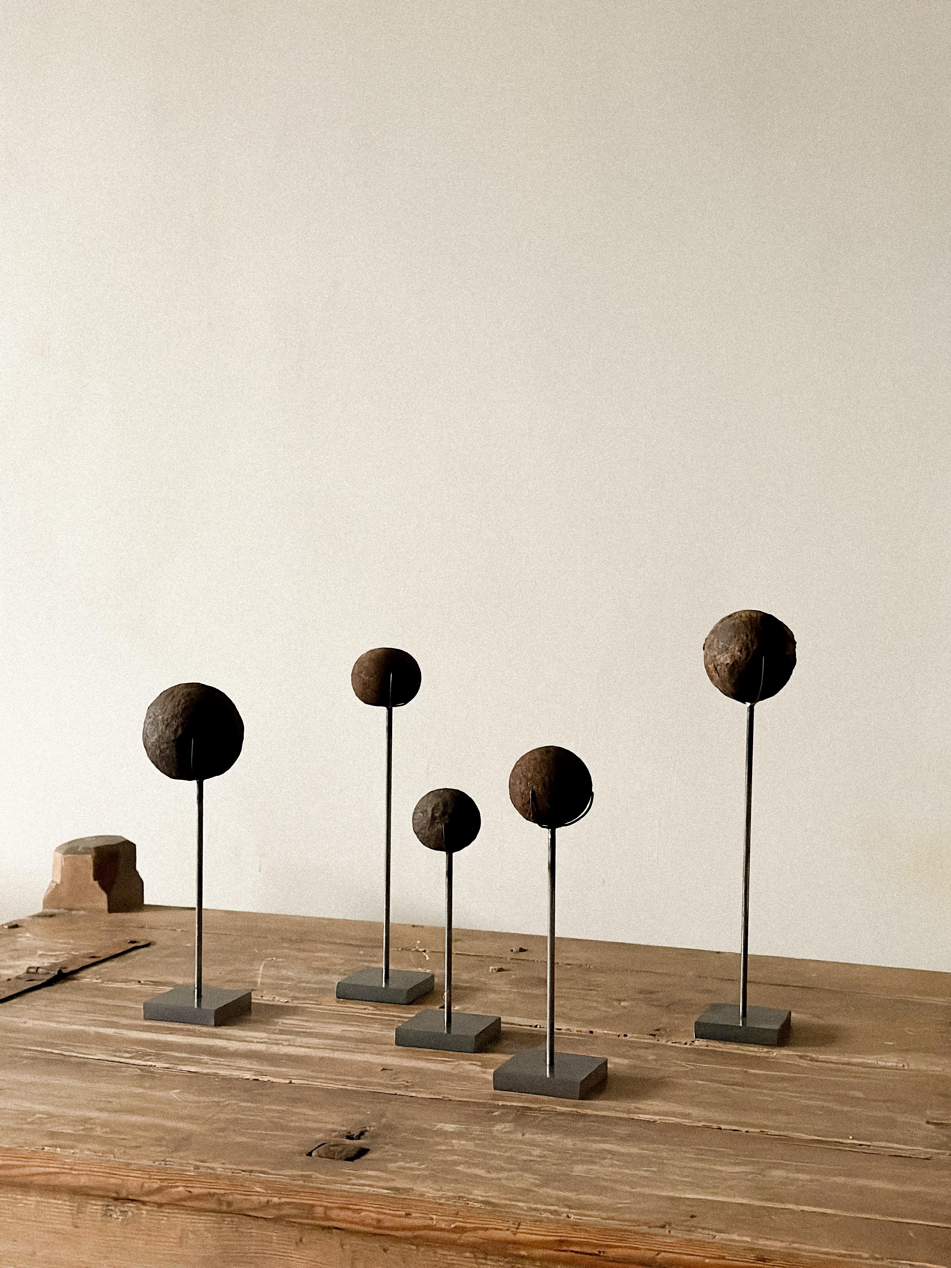 A set of antique iron cannonballs originating from an old Norwegian fortress, dating to the 1800s. Mounted on custom-made metal stands for display. Surface wear and patina consistent with age. Each piece varies in shape and texture with beautiful