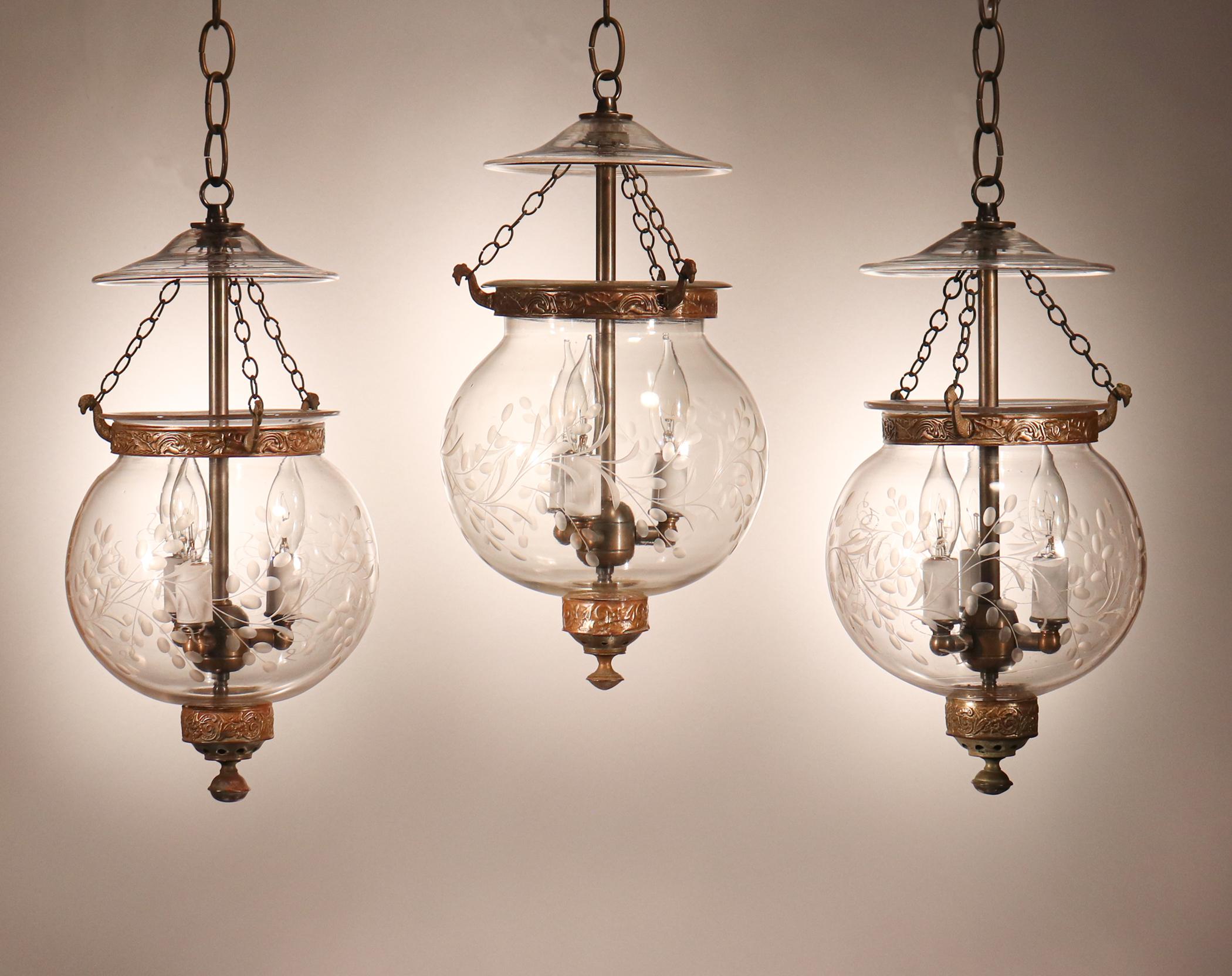 A rare find, this suite of three circa 1880 English globe lanterns feature superb quality hand blown glass replete with desirable air bubbles and swirls. The antique globes feature a finely etched vine motif. Note that there is a very slight