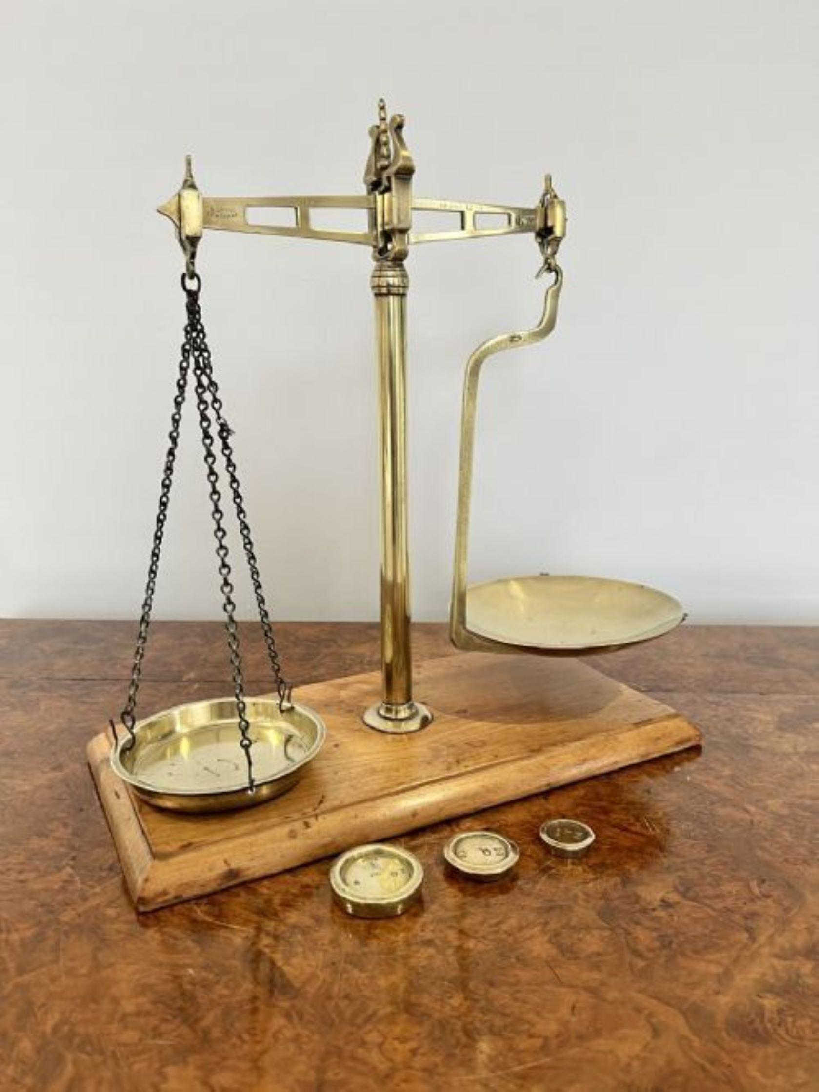 Set of antique Victorian brass scales standing on a mahogany base, with a brass centre column having a shaped brass arm holding a removable brass bowl and a brass removable bowl on three chains with a set of brass weights 