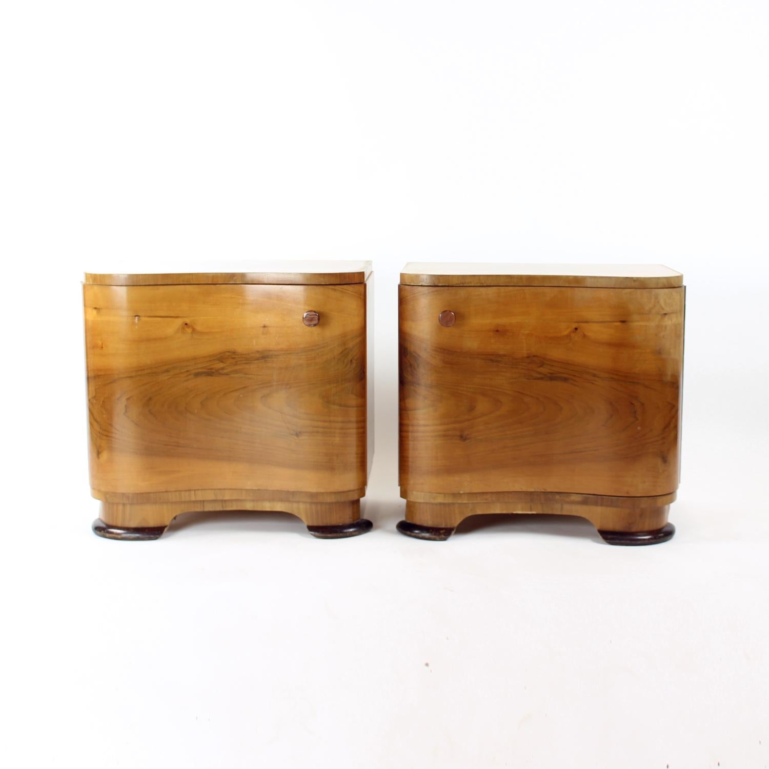 Set of two beautiful bedside tables from the art deco design era. The tables have a wonderful presence because of the curved shape of the front side and door, as well as because of the wonderful walnut veneer. The tables are made of walnut wood and