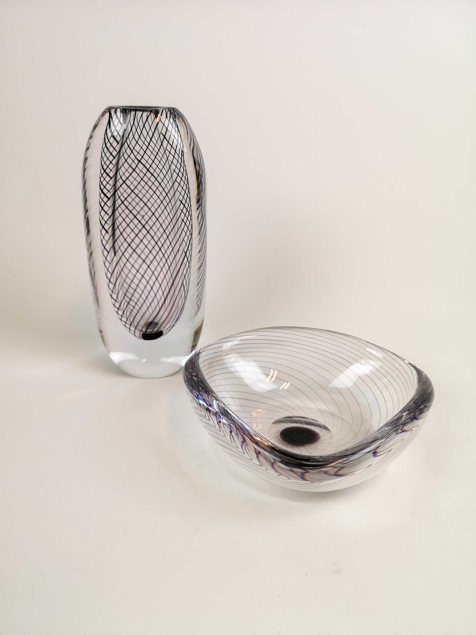 A set of one art vase and one bowl produced in Sweden at the Kosta factory. Designed by Vicke Lindstrand. 
The pieces are made of clear glass with black (aventurine) glass threads.

Signed on the floor with 