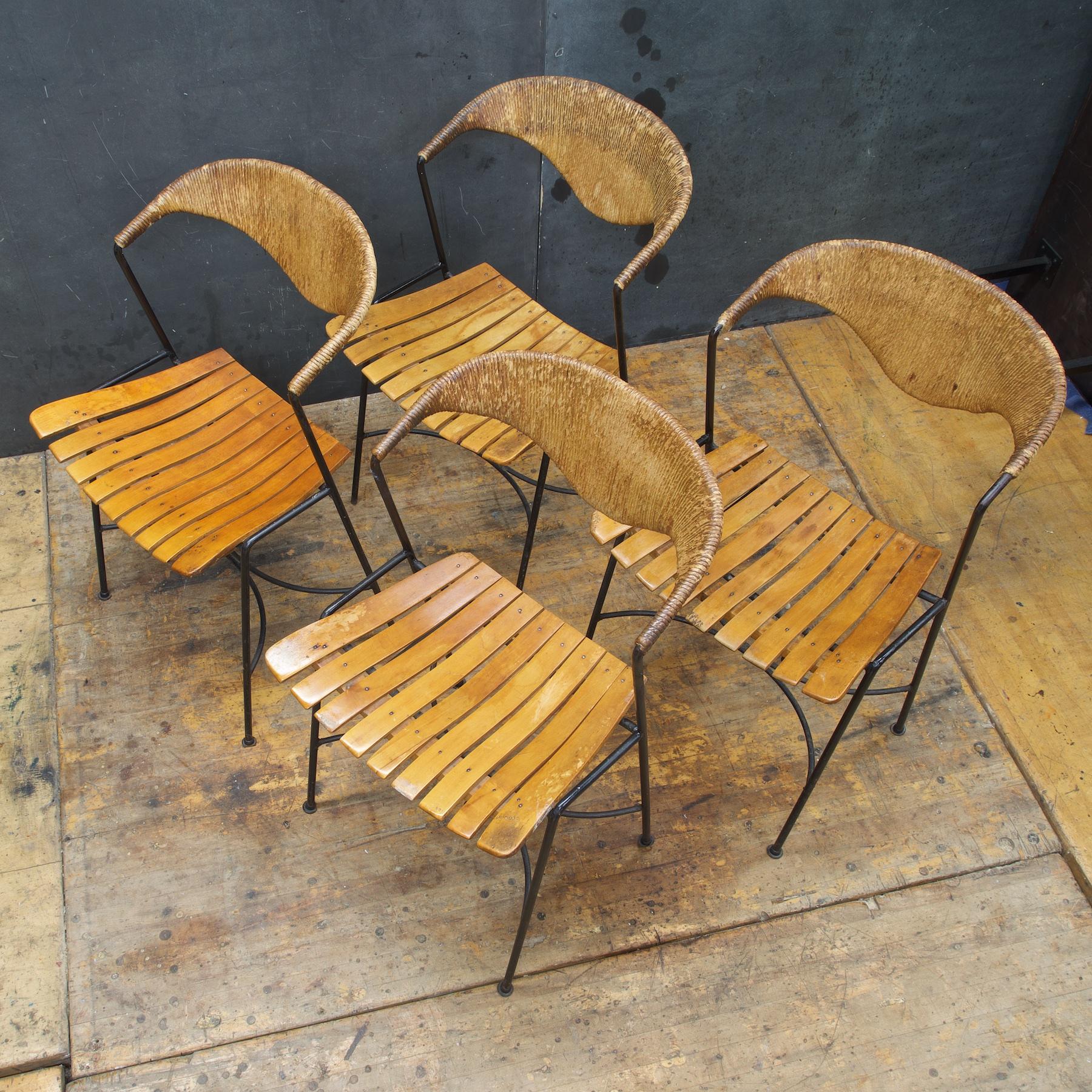 Set of four. Wrought iron frames with wood slat seats and sculpted papercord backrests. Some of Wooden slats showing wear and loss. One small bit of rush missing. Rare design. Measures: Arm heights are 29 inches.
 