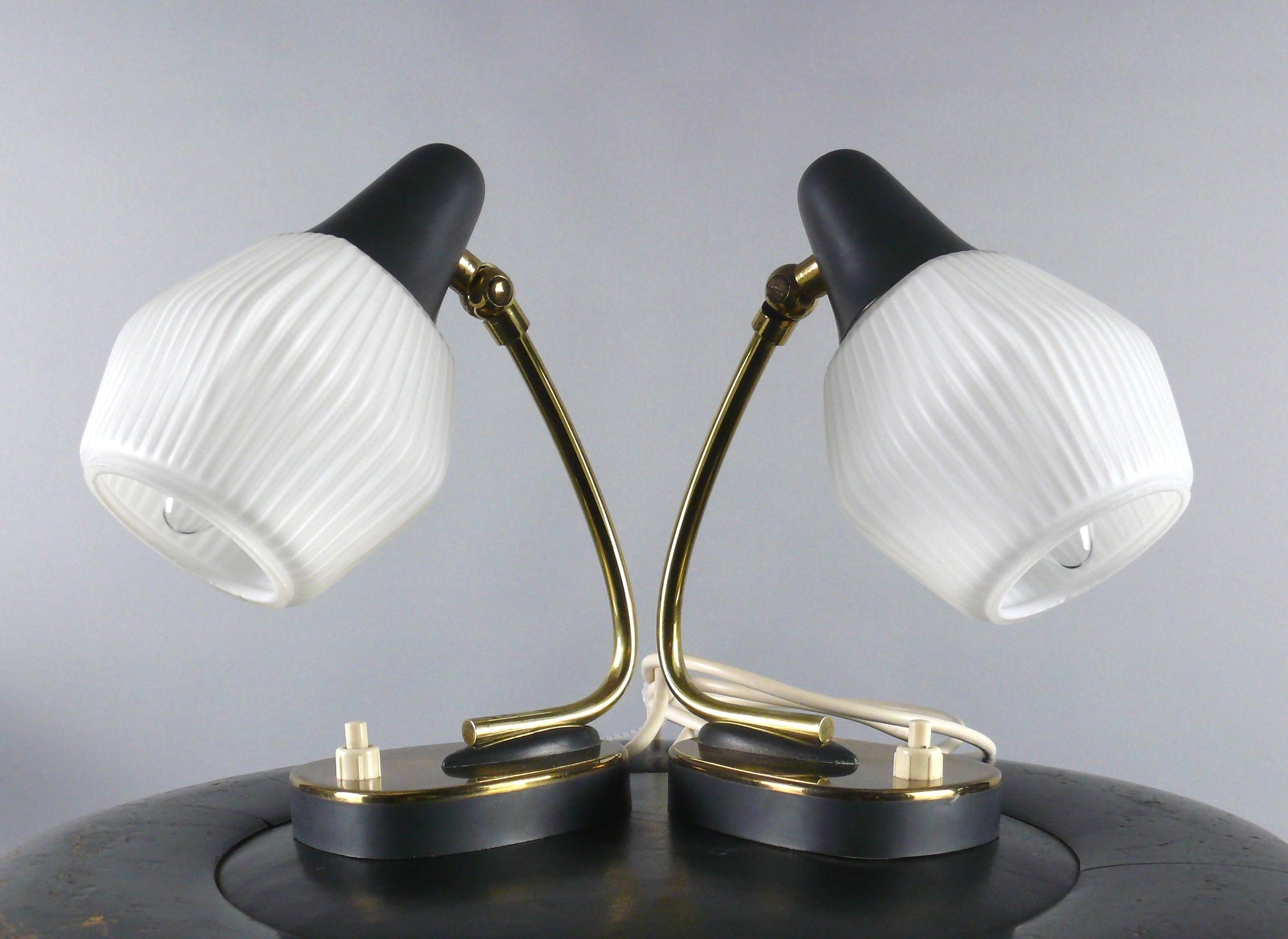 Two bedside lamps made in Germany in the 1960s . The lamps have an opaline glass lampshade and a design which contrasts between dark grey and brass areas. The lampshades can be adjusted with a joint. The lights are switched on and off via a switch