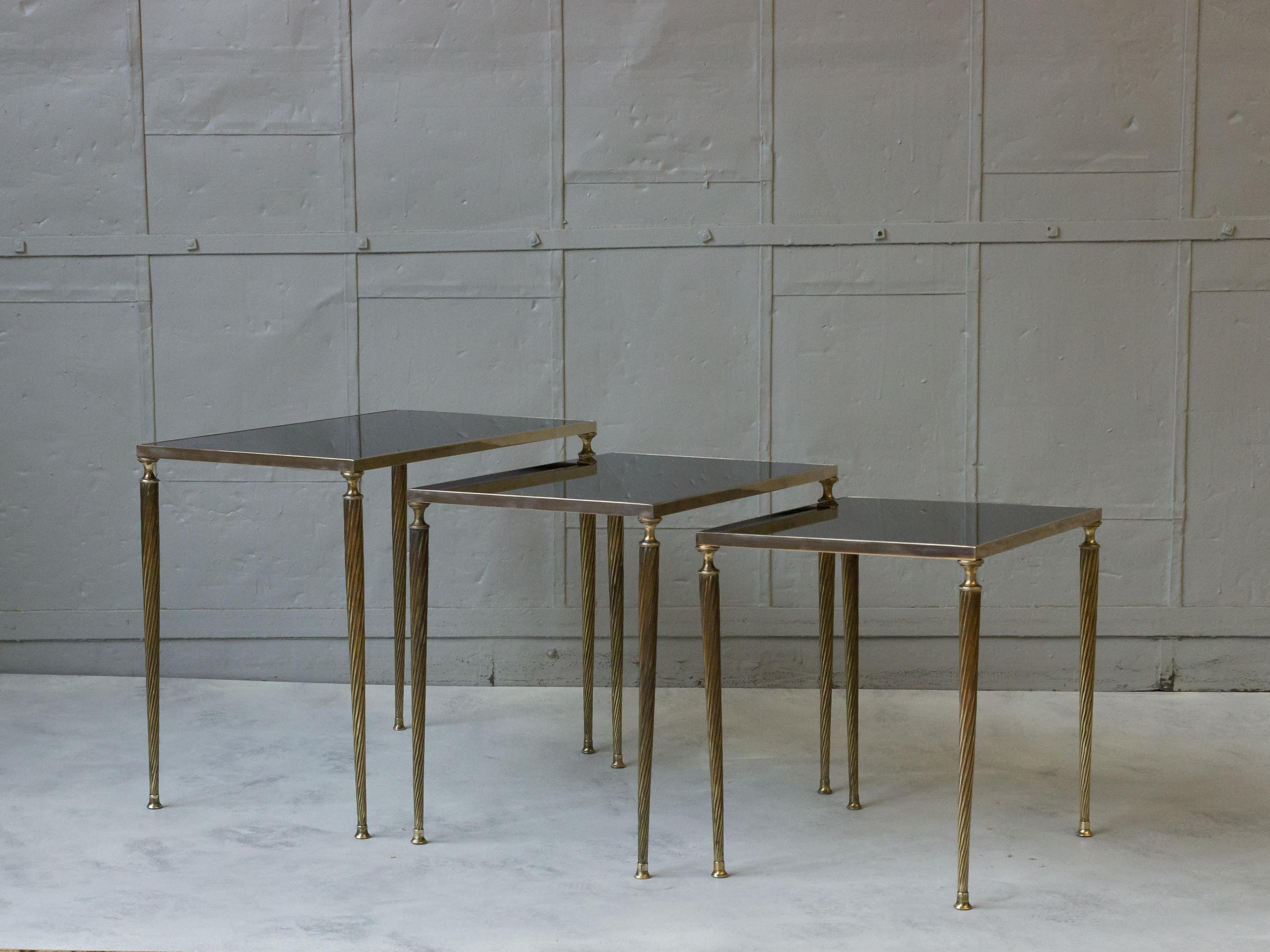 This set of three French nesting tables is a beautiful blend of black glass and brass, reflecting the distinctive style of Maison Jansen. Dating back to the 1940s, these tables feature spiral turned brass legs and frames that beautifully complement