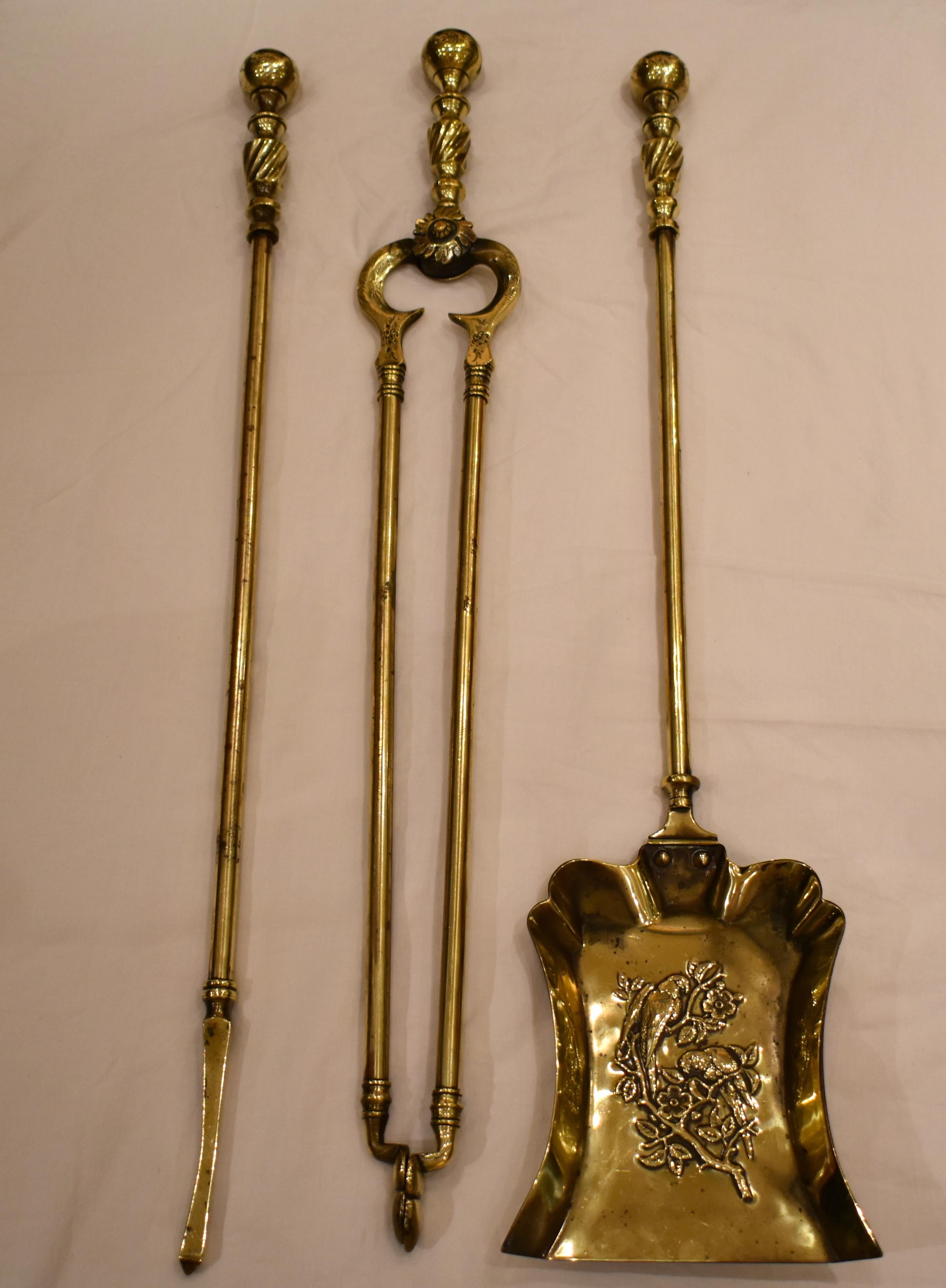 An extraordinary matching set of three mid-19th century English solid brass fire tools having suppressed ball finials with floral pattern vectors. The shovel entails a unique illustration of a pair of exotic birds on a branch, with all three pieces