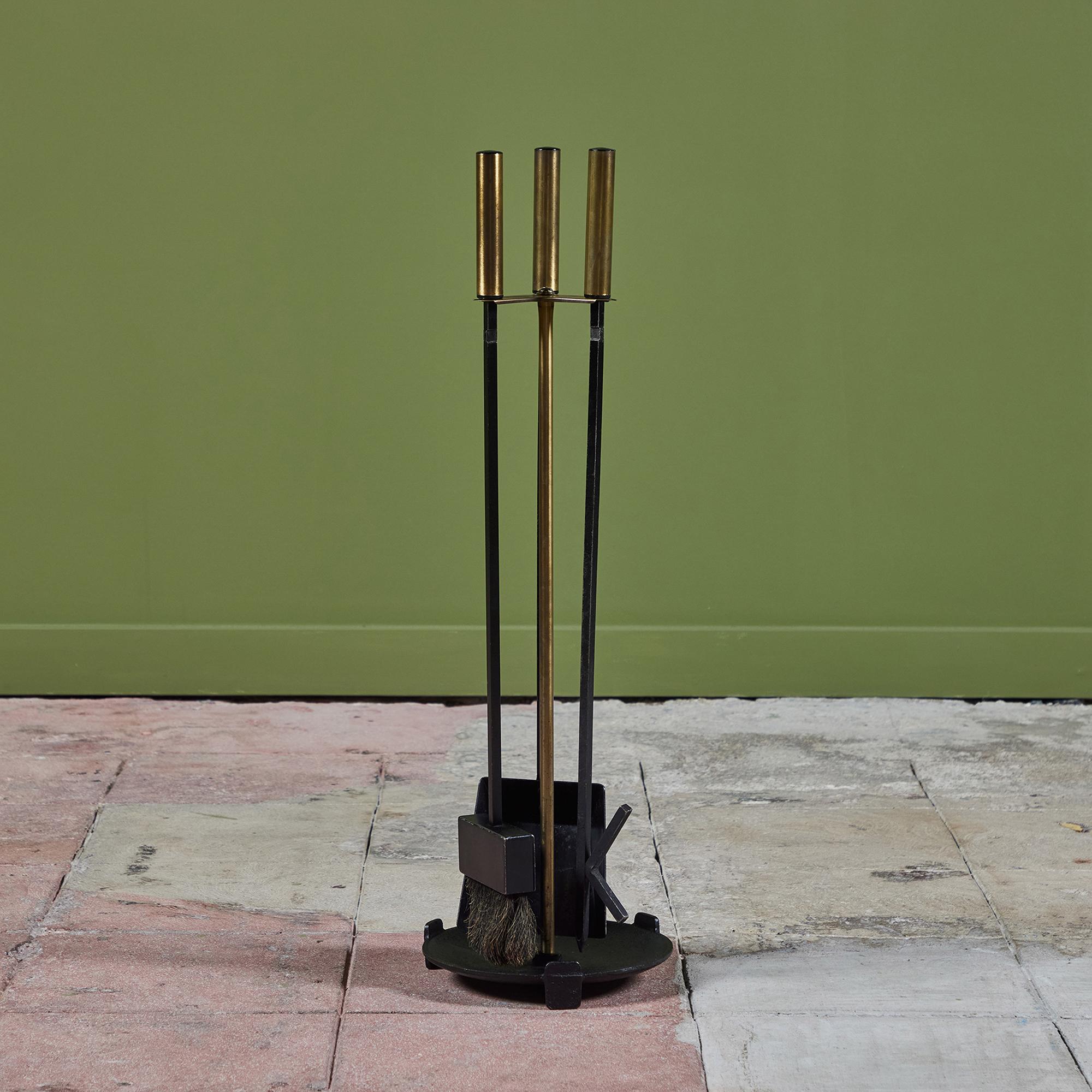 Three piece set of fireplace tools with stand. The set features three tools with cylindrical brass handles and matching rounded stand. All elements are made of blackened iron. This modernist piece shows off clean and minimal lines perfect for any