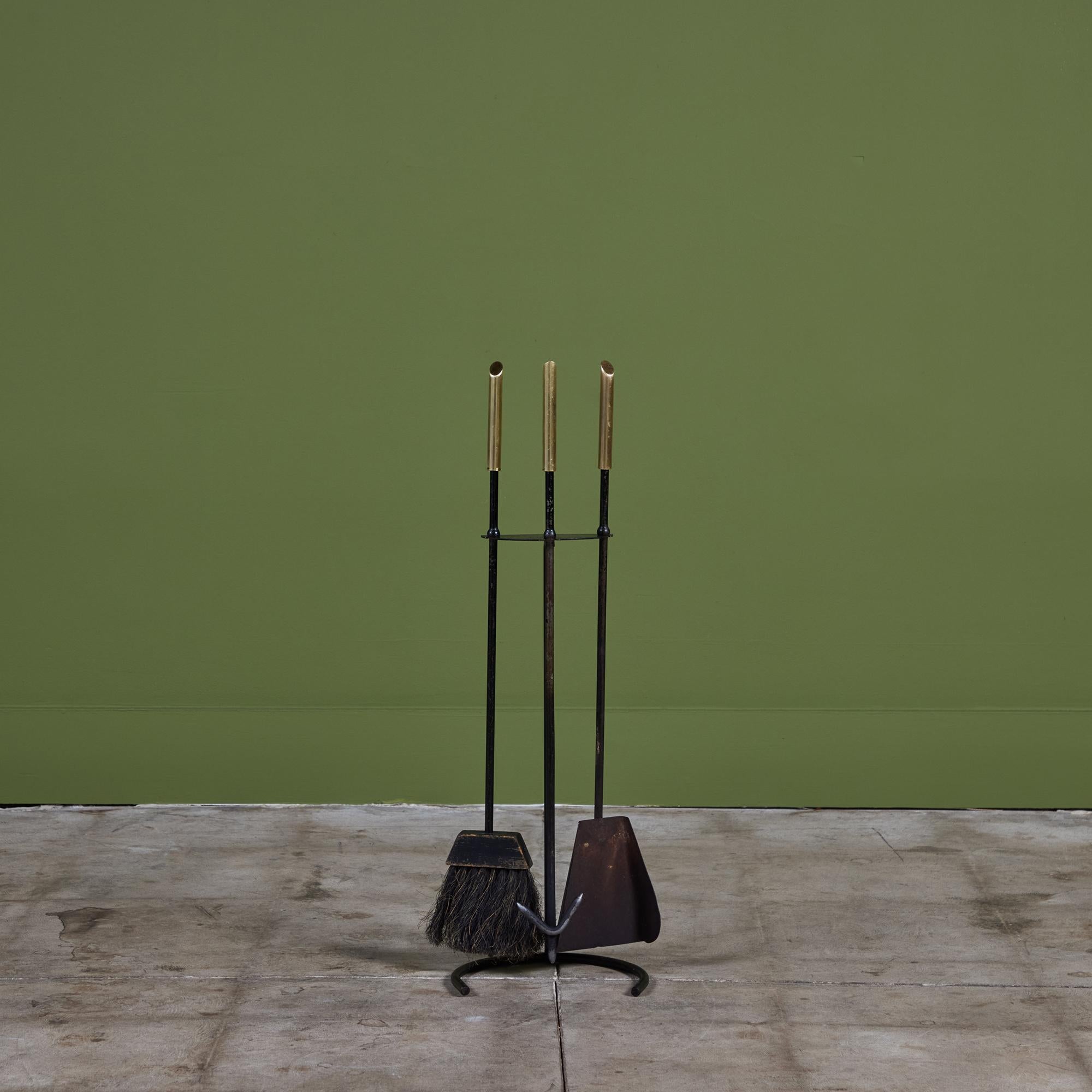 Set di tre attrezzi per caminetto con supporto. Il set è composto da tre utensili con manici in ottone e supporto con attacco a semicerchio. Tutti gli elementi sono realizzati in ferro annerito. Questo pezzo modernista sfoggia linee pulite e