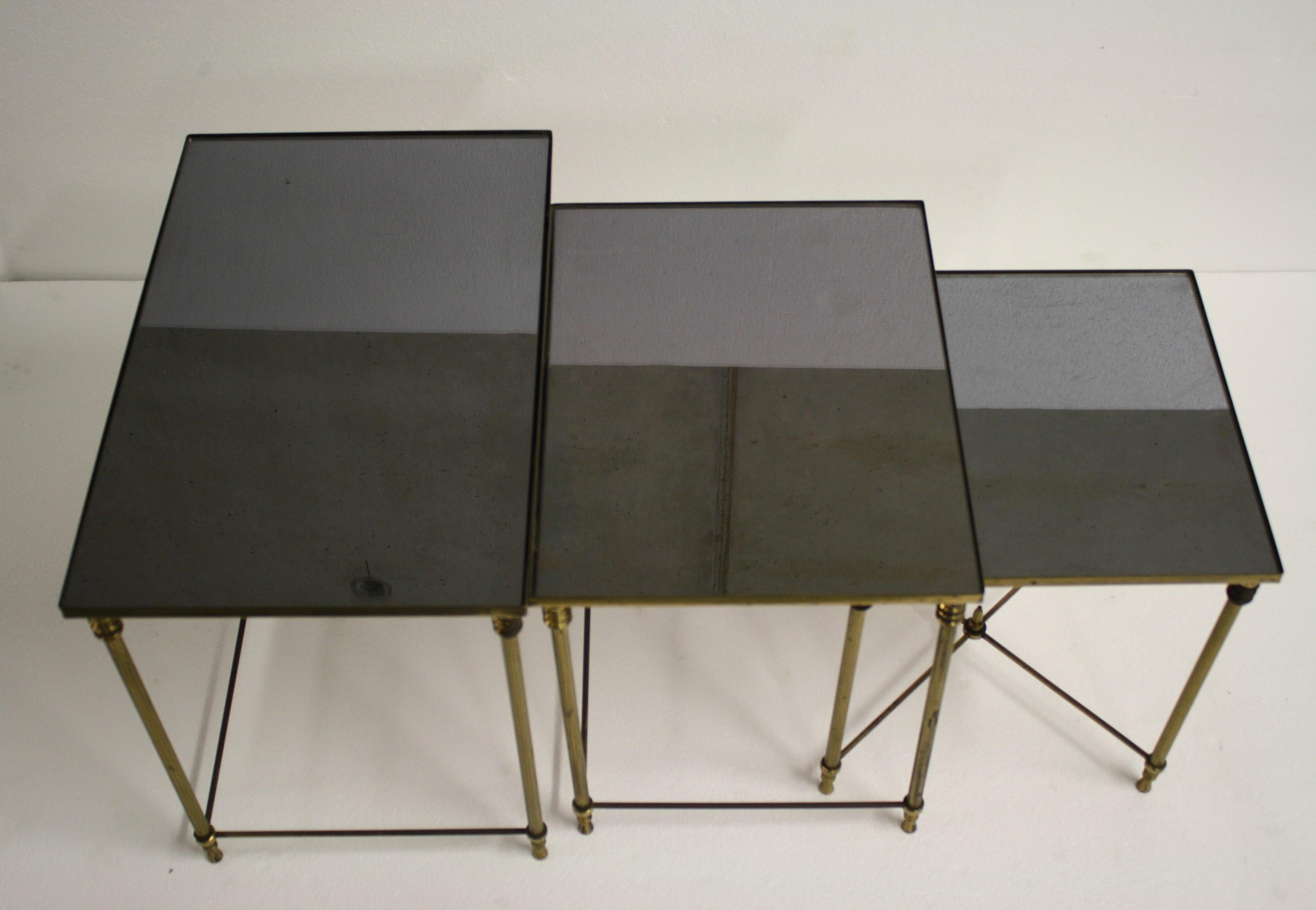 Lovely set of brass neoclassical nesting tables in the style of Maison Baguès.

The tables are made of patinated brass and reeded legs with smoked glass tops.

The frames have some lovely details and is in overall good condition.

Note that