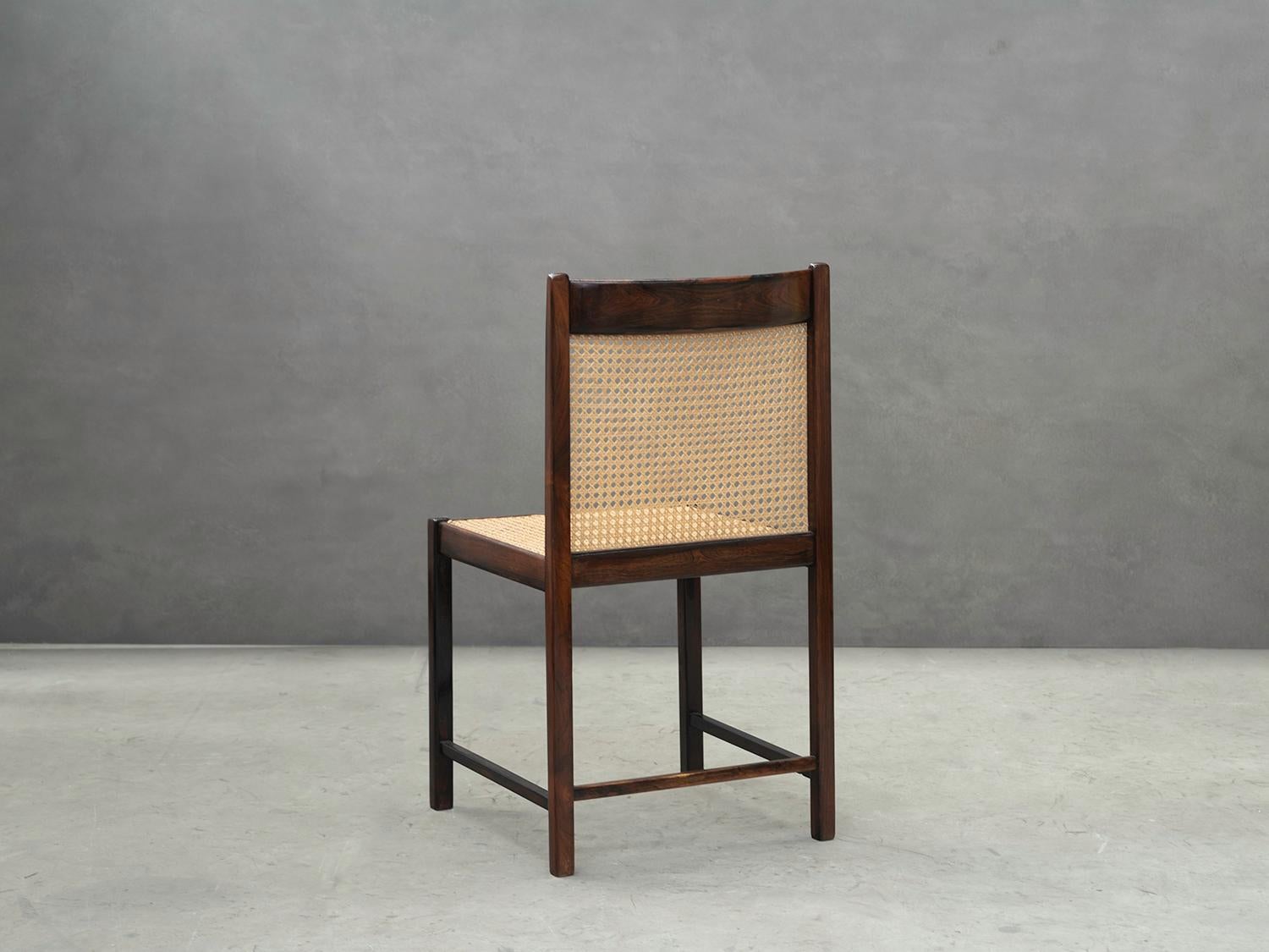 The set of six Brazilian Mid-Century Modern dining chairs are made of rosewood (Jacaranda) and cane seat.

The structure has a square section design with four feet, made in solid rosewood. 

The curved backrest is composed of rosewood and cane,