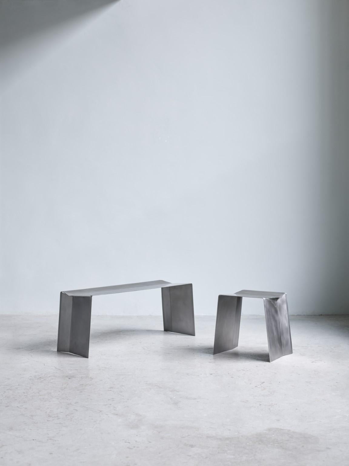Set of camber stool and bench by Paul Coenen.
Dimensions: 
Stool: W 47 x D 37 x H 45 cm
Bench: W 118 x D 37 x H 45 cm
Materials: Stainless steel.

The Camber bench and stool originated from the IDEA of manufacturing a piece of furniture from a