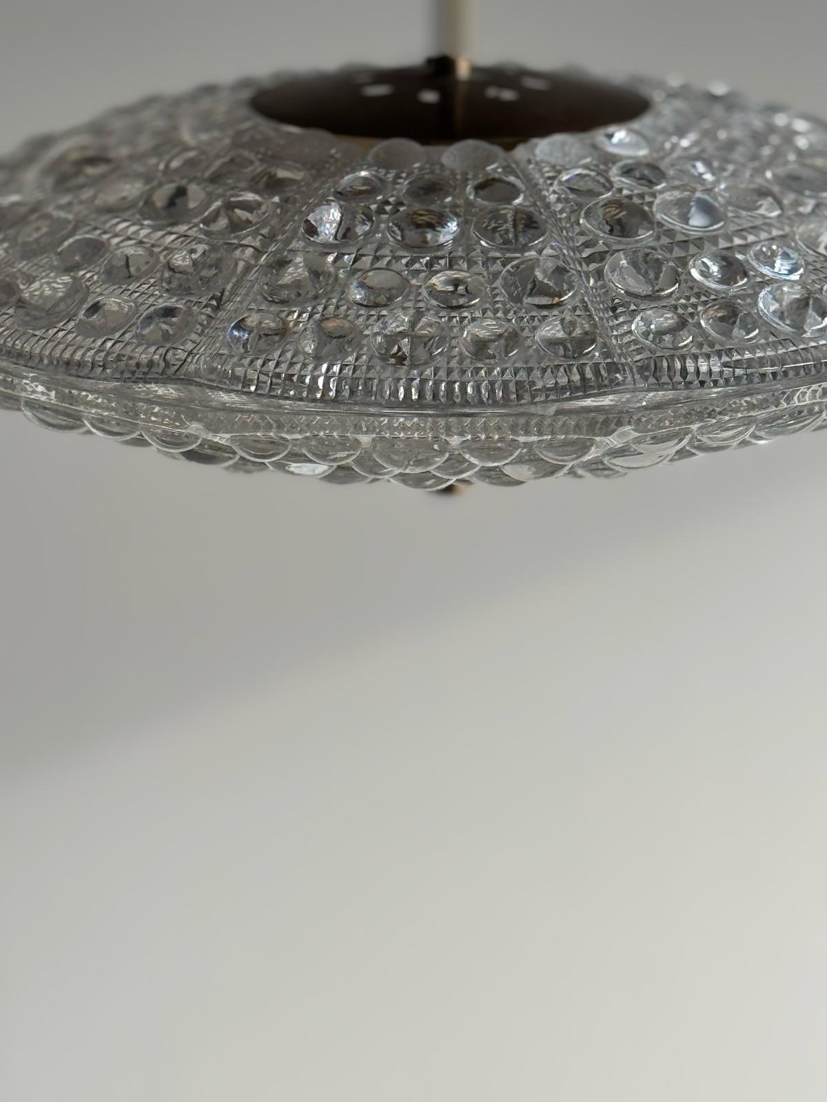 A refined Scandinavian pendant light designed by Carl Fagerlund for Orrefors and produced by Lyfa in Denmark during the 1960s. The piece features a circular textured glass diffuser with a sculptural, bubble-like surface that beautifully refracts