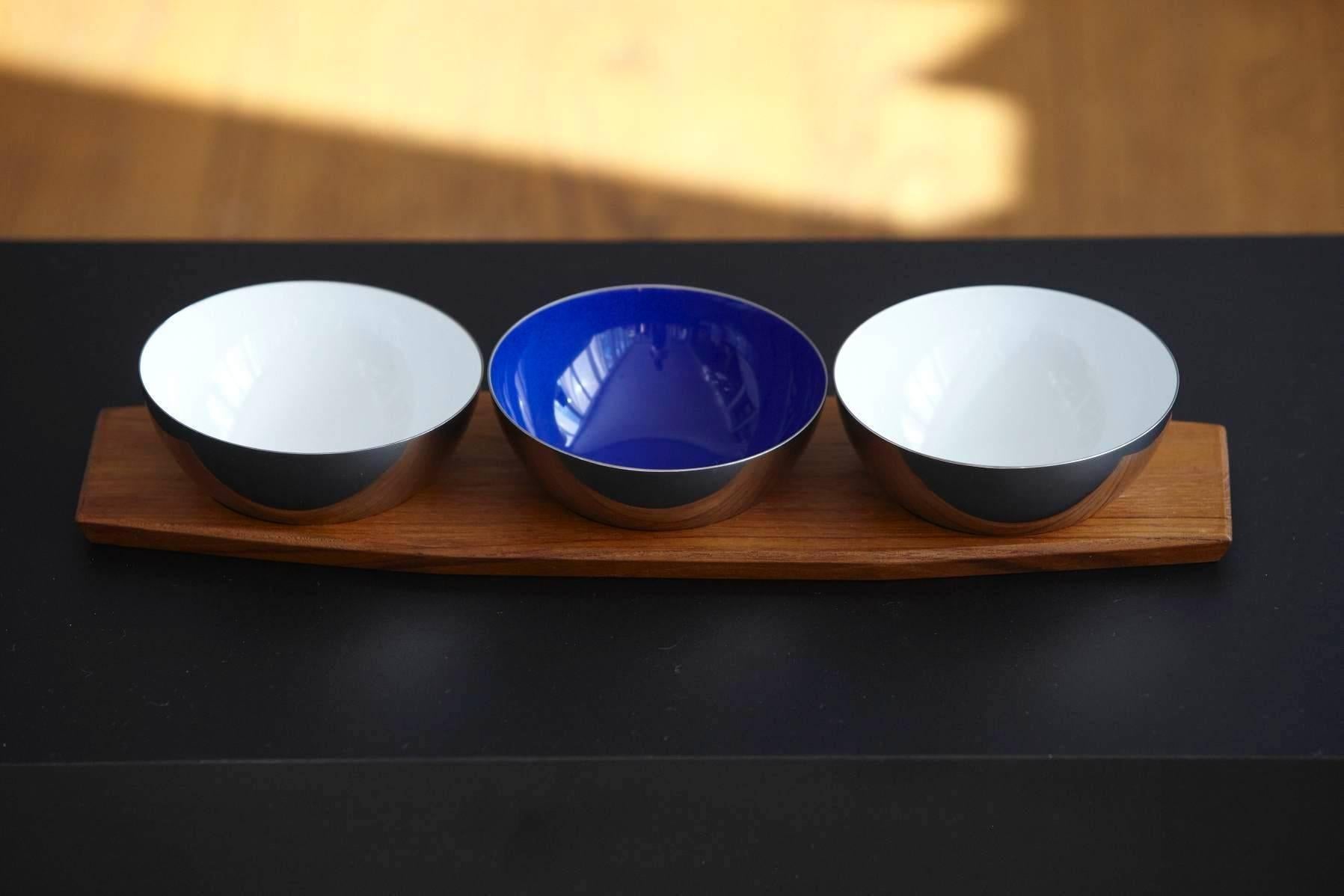 Beautiful set of three Cathrineholm of Norway silver buffed stainless steel of highest quality and porcelain enamel bowls in white and cobalt blue on a teak tray.
Designed by Grete and Arne Korsmo. 
Grand Prix X Triennale in Milan, 1956 and Gold