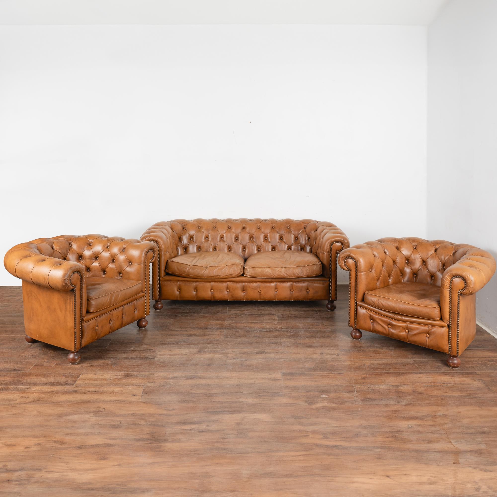 Set (3) vintage leather Chesterfield style 2-seat sofa and pair of club arm chairs.
The camel brown leather has traditional tufted buttoned accents, rolled arms, nail head trim, and hard wood bun feet.
Sold in used vintage condition. Cushions have