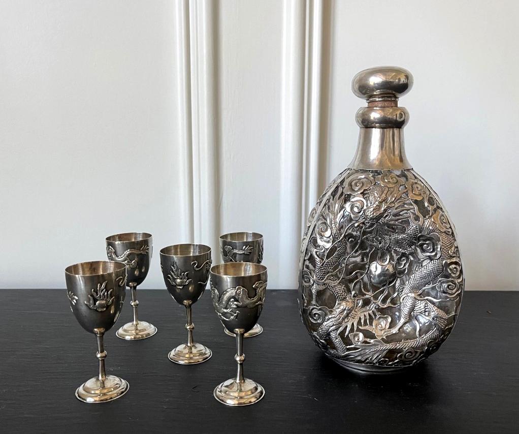 A set of Chinese Export silver drinking set consists of a pinch bottle and five cordials circa 1910s-1920s. Featuring matching elaborate chased relief dragon and cloud motif on surface, this is an rare set of this form by the 