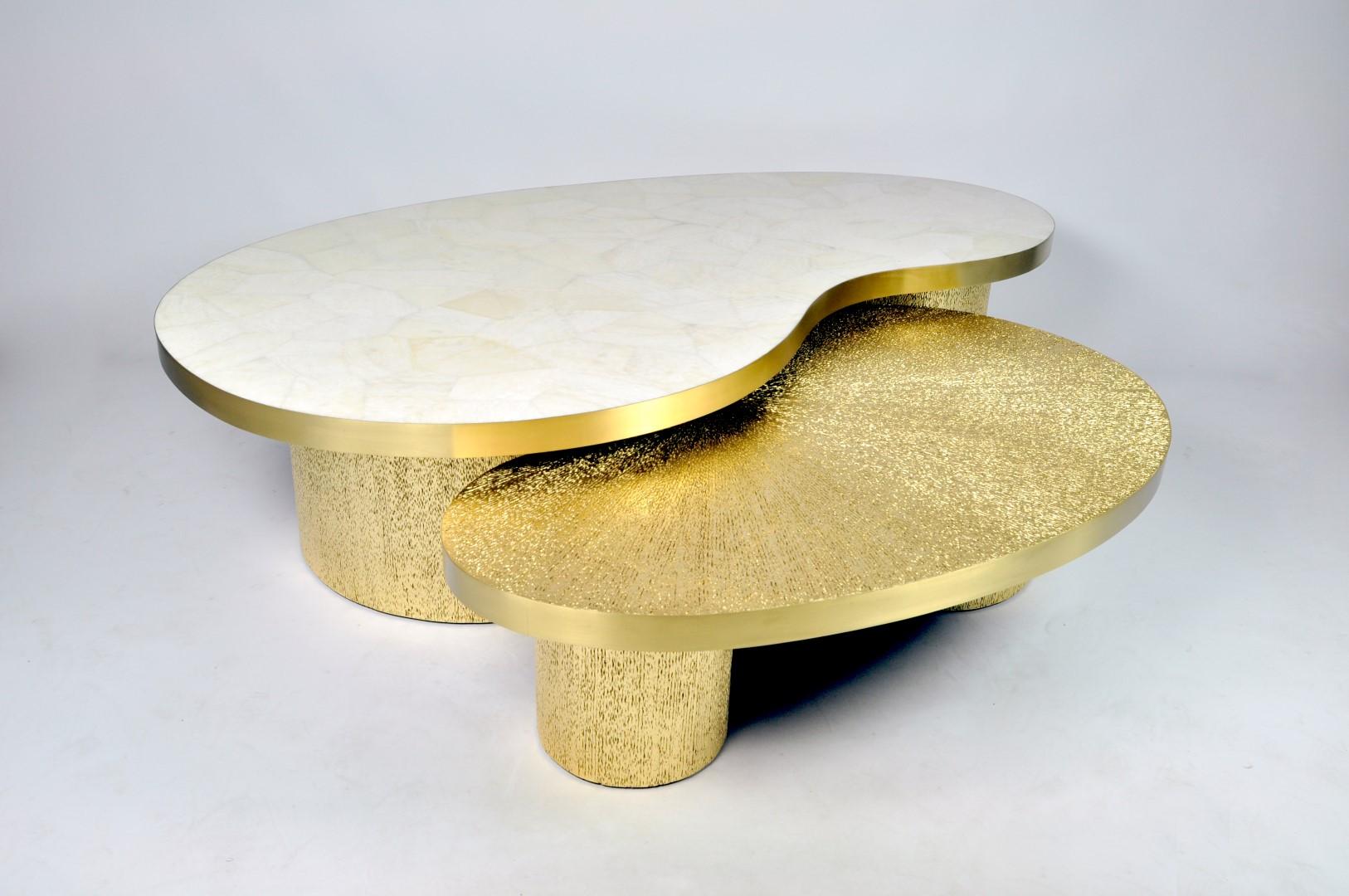 This set of 2 coffee tables with a bean shape is made of various materials.
The highest table has a top in white rock crystal and the lowest table has a top in gilded vegetal fiber marquetry.
Both tables tops have edges in brushed brass.
The two