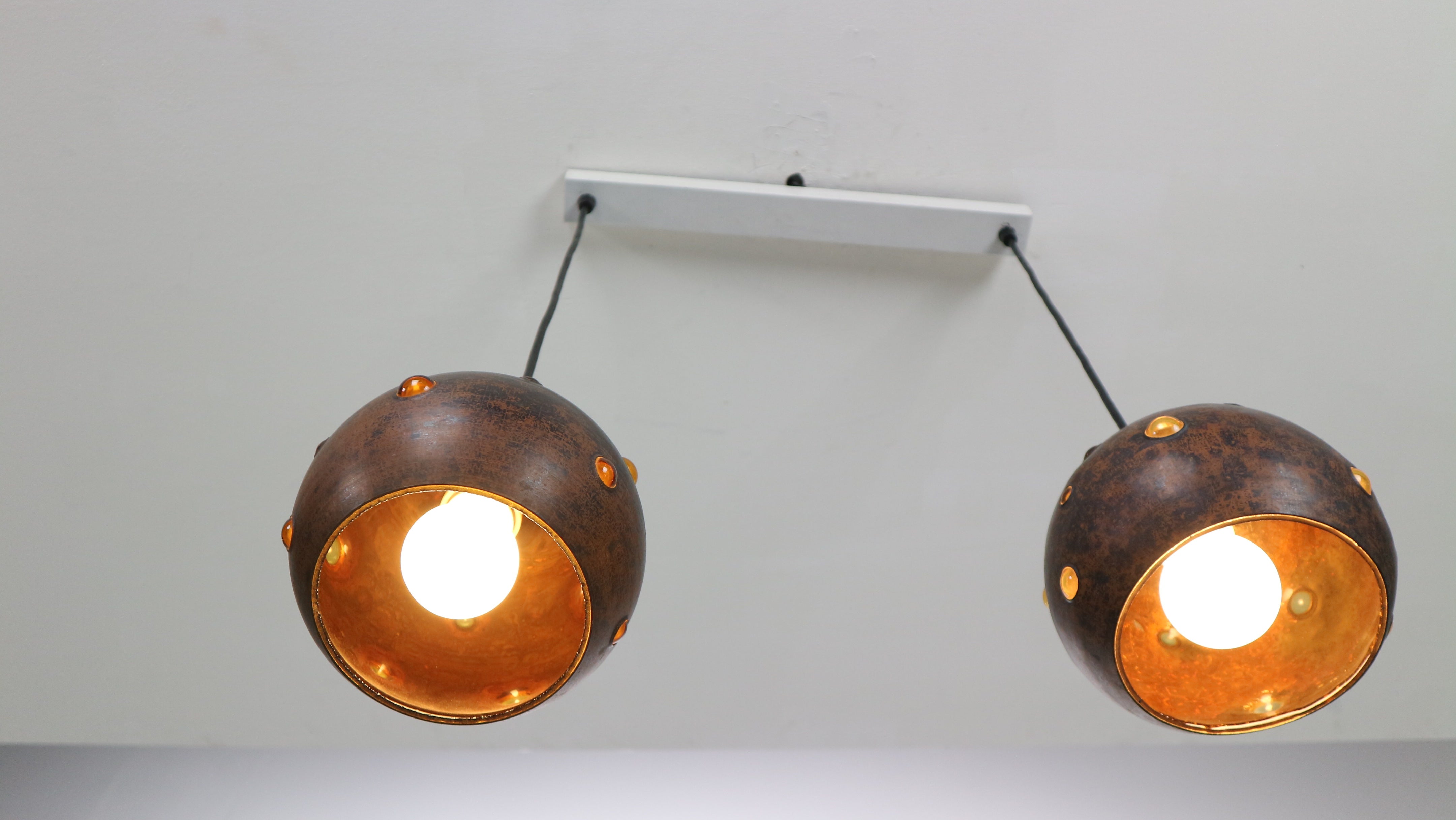 These unique pendants are Mid-Century classics by one of the important modern finnish designers. Nanny Still designed for RAAK in the 1950s-early 1960s. These lamps are perforated 8 inch diameter copper spheres lined with amber handblown glass.