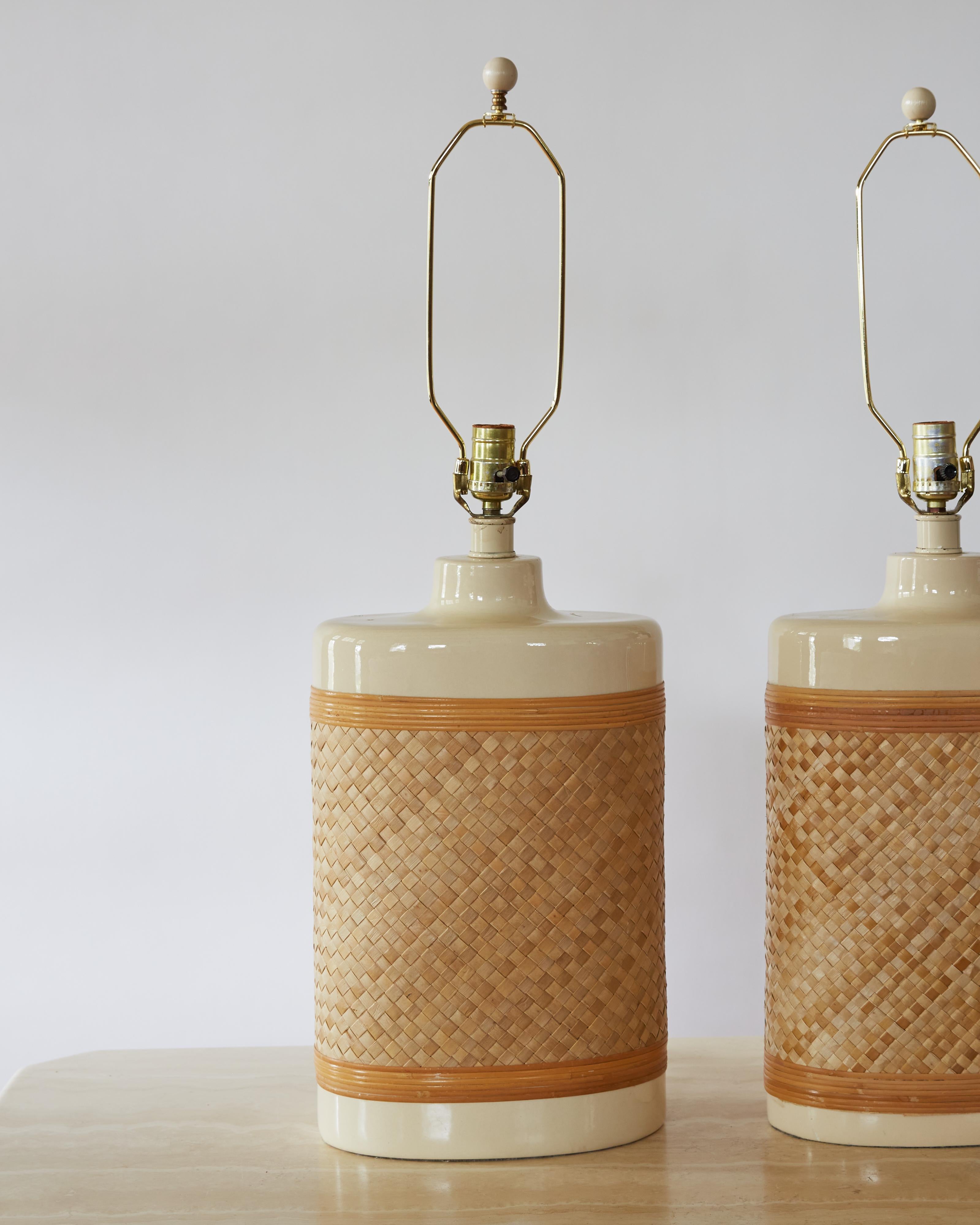 Introduce some coastal flair to a bedroom, living room, or den with this pair of vintage lamps. Oval in shape, the large body of the lamp is made of a cream-colored ceramic wrapped in woven raffia, and topped with a brass harp and finial. Wired for