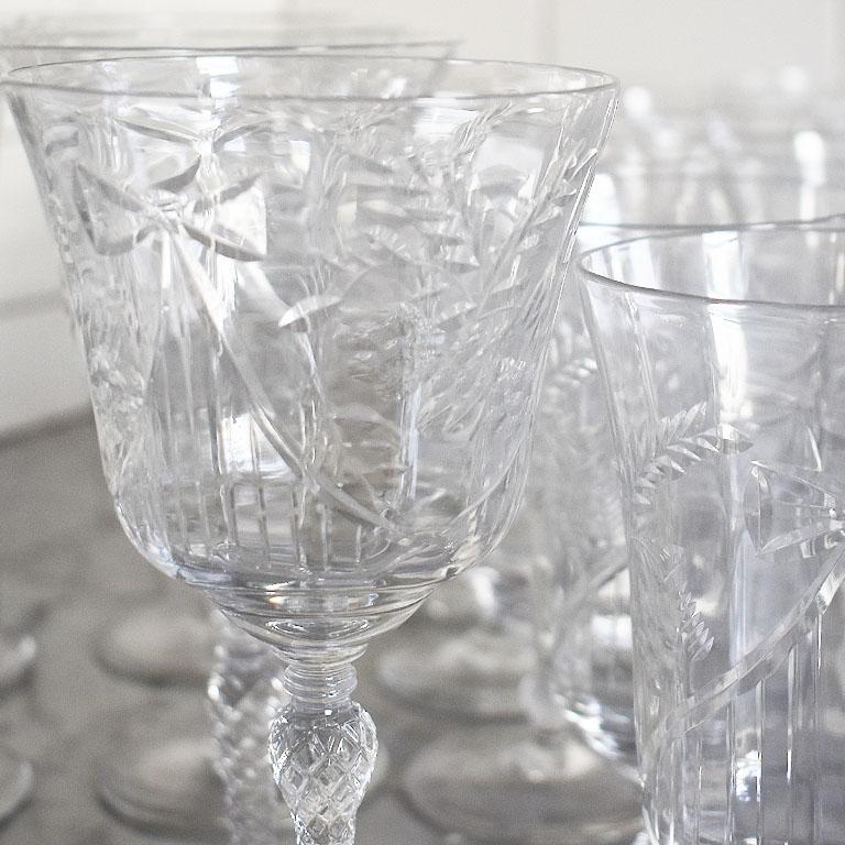 A set of 30 crystal ribbon motif drinking glasses. This set includes eight wine goblets, 12 tea glasses, and 10 coupe champagne glasses. The stems are faceted and on round bases. The bodies of the glasses feature a raised ribbon motif.