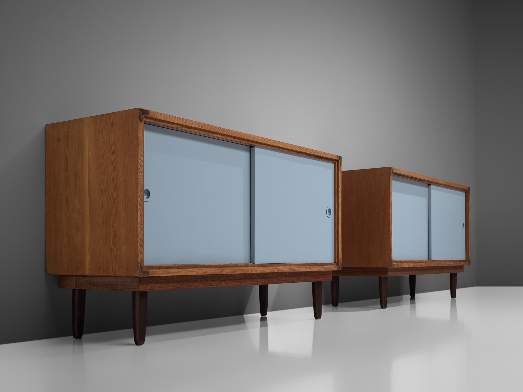 Danish solid pine cabinets with blue sliding doors, Denmark, 1950s

These cabinets show a basic design, with a rectangular front placed on tapered round legs. Due to the legs it has a light appearance. 
The warm expression of the wood nicely