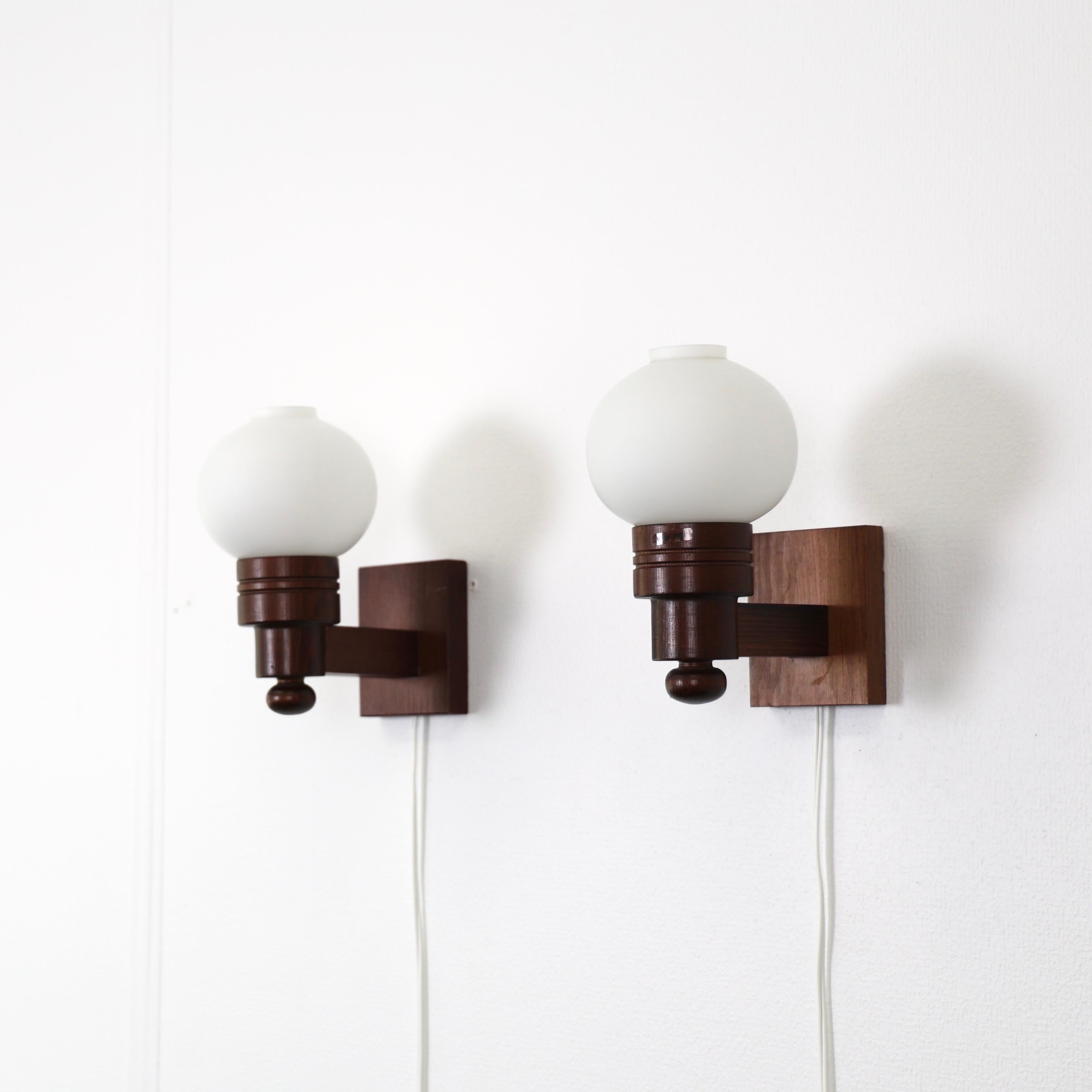 A set Dark Stained Swedish Modern Pine wood Wall lamps made by Aneta in the 1970s. A fine Scandinavian duo. 

* A pair (2) of wall lamps in dark stained pine wood with white round glass shades
* Manufacturer: Aneta, Sweden
* Year: 1970s
* Condition: