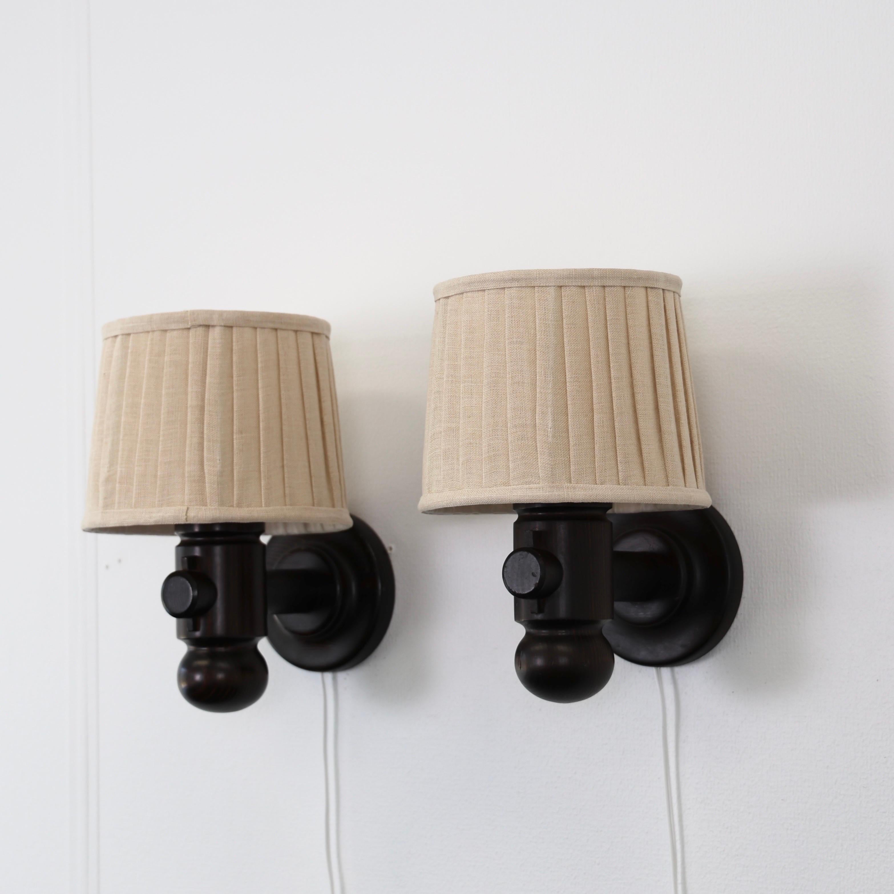 Set di lampade da parete in legno di pino tinto scuro disegnate da Jan Wickelgren per Aneta negli anni Settanta. Un bel duo scandinavo. 

* Coppia (2) di lampade da parete in legno di pino tinto scuro con paralume in tessuto beige.
* Designer: Jan