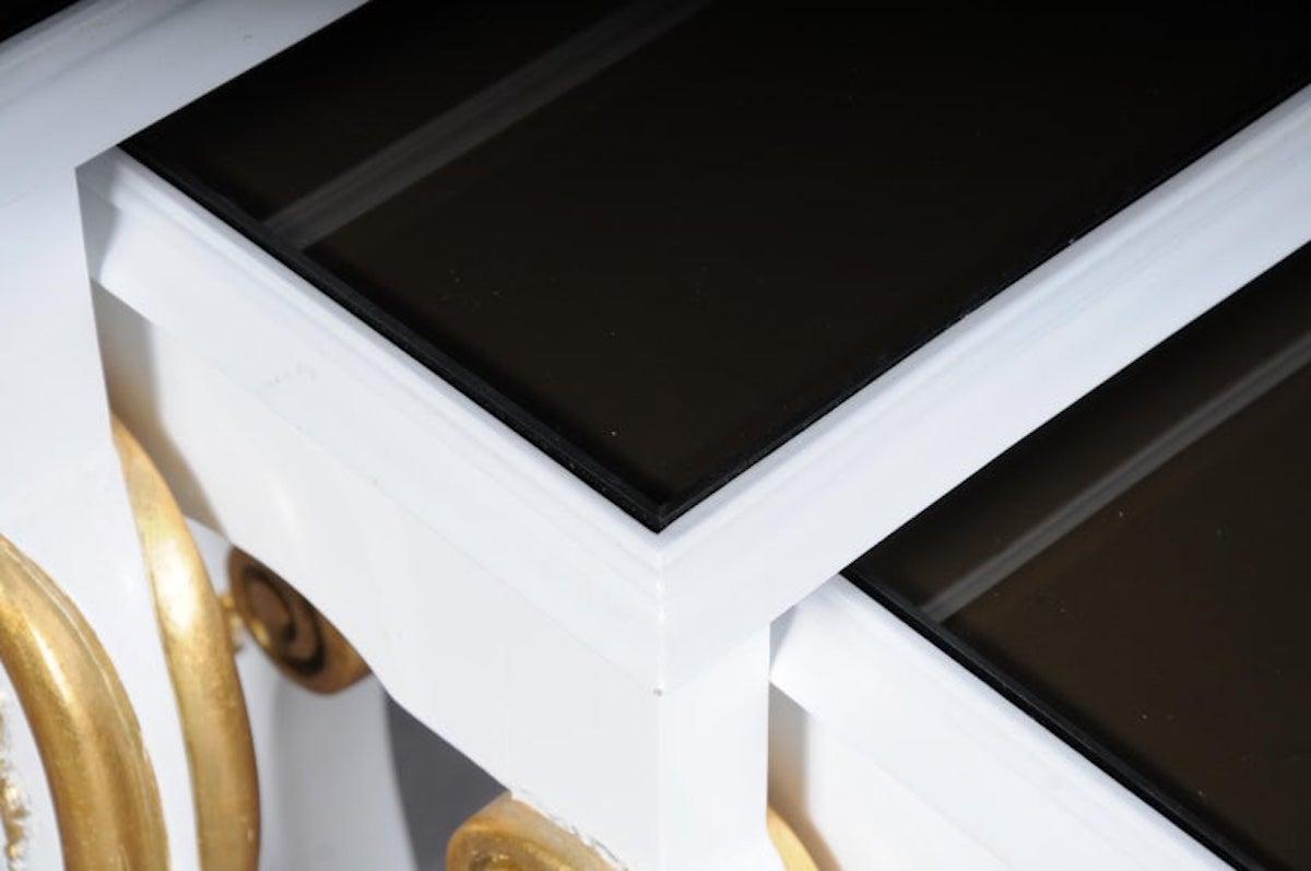 Set de 3 tables d'appoint design de style Empire.

Bois de hêtre massif peint en blanc et partiellement doré. Cadre incurvé sur de longs pieds frisés Pris blanc. Plateau en verre épais teinté noir. Les tables d'appoint sont disposées en gradins et