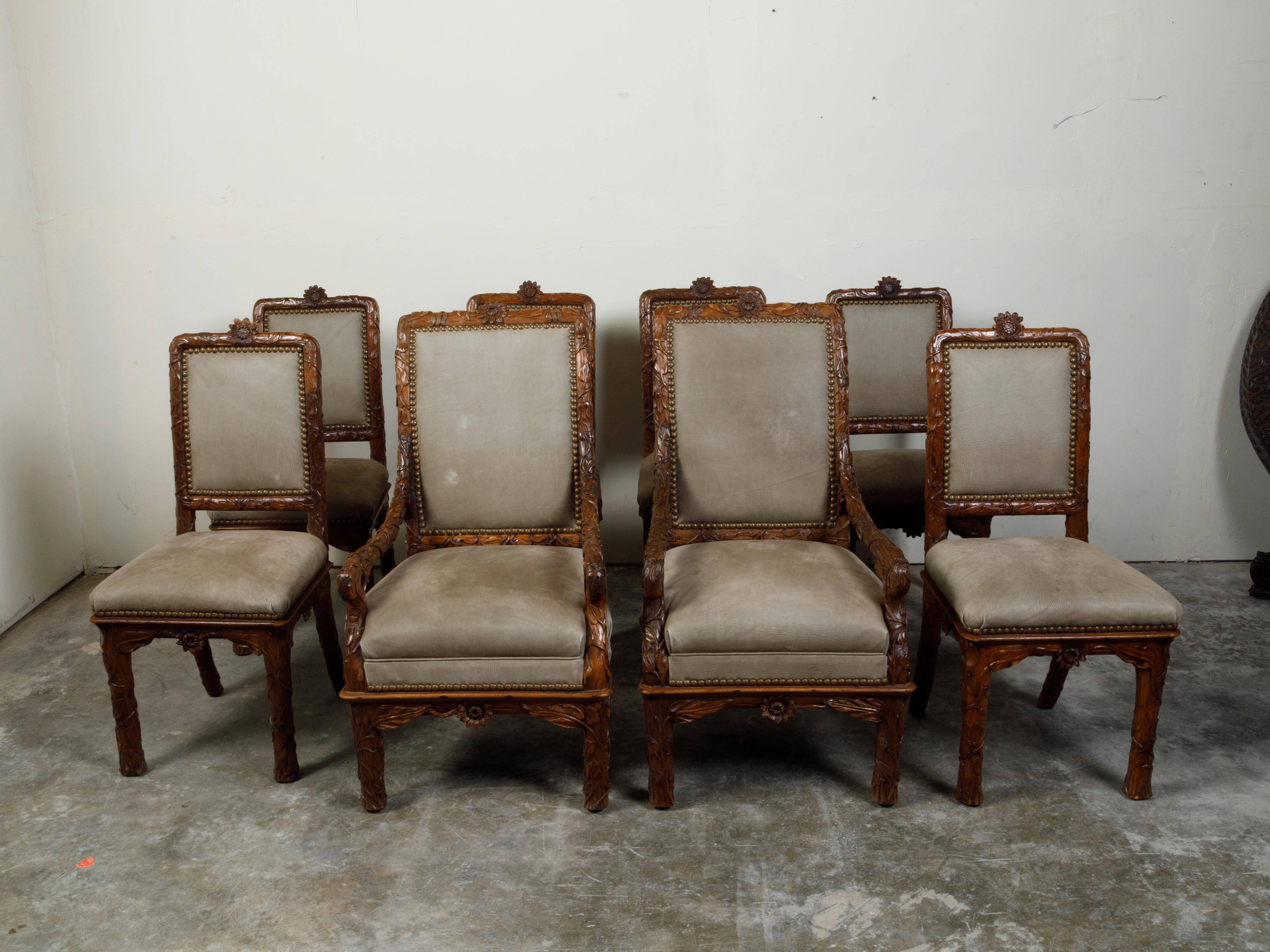 A set of eight Black Forest dining room chairs from the early 20th century, with carved foliage décor and upholstery. Created during the first quarter of the 20th century, this set of dining room chairs features two arms with large scrolling accents