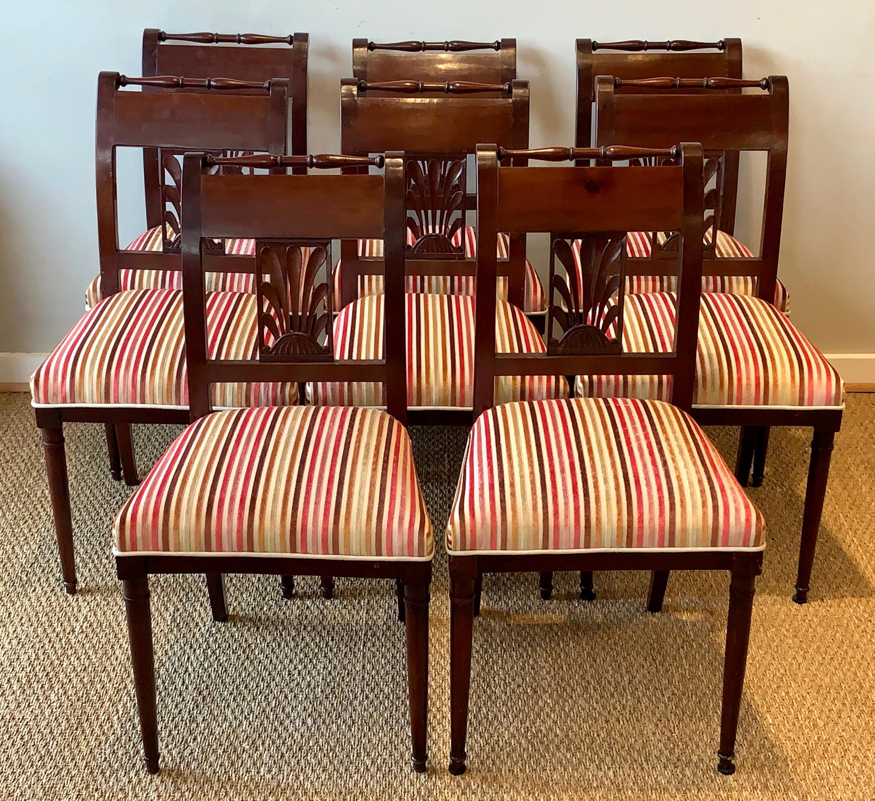 An elegant set of eight late 19th century Directoire style carved mahogany dining chairs comprising all sides. The delicately turned rail rests above a stylized carved acanthus leaf splat resting on round tapering legs. The chairs are newly
