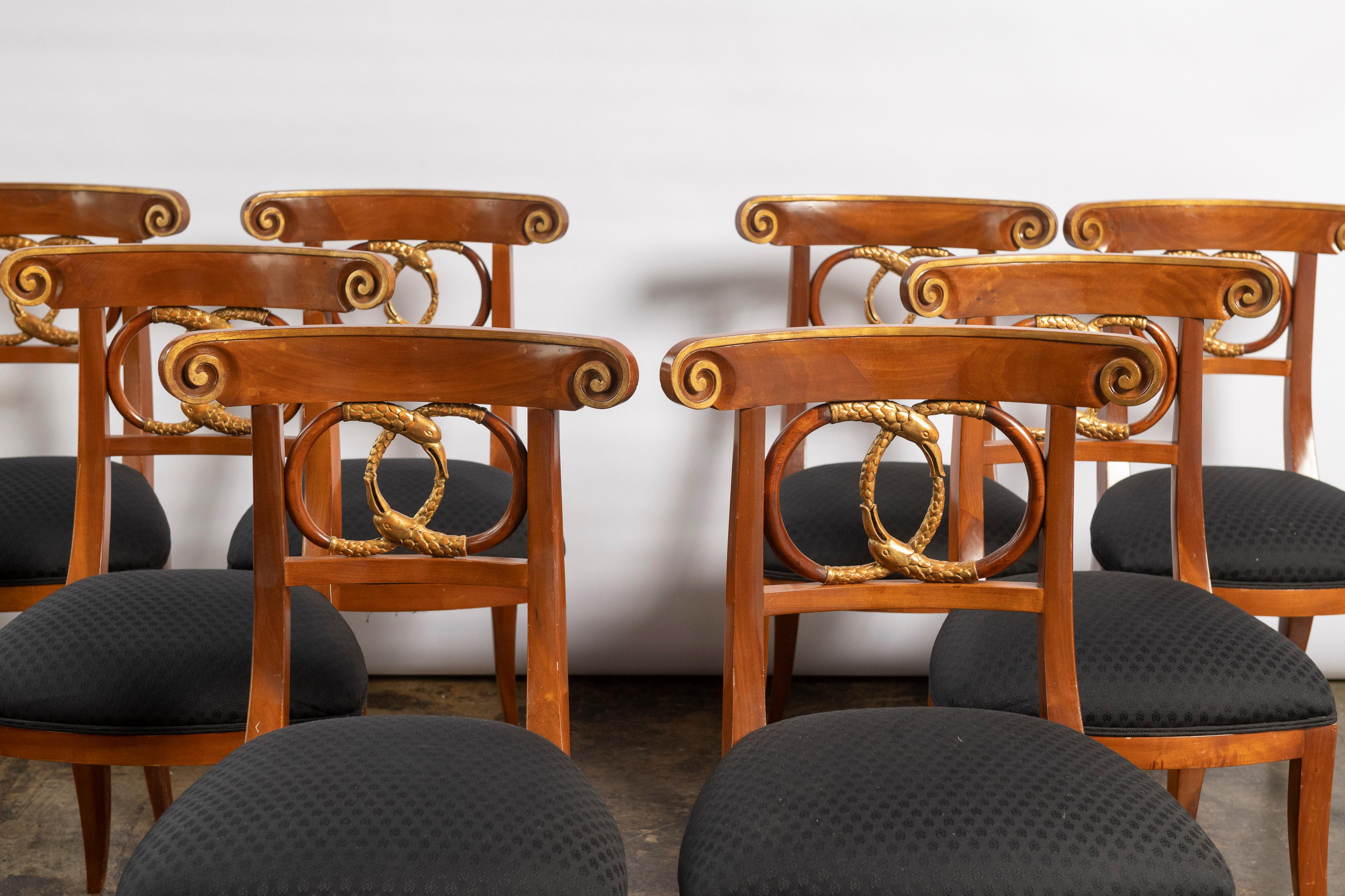 Set of eight beautifully proportioned mahogany dining chairs in the Biedermeier style made by Burton-Ching. The chairs have graceful sloping outward legs, a backrest of carved intertwined serpents in a double circular pattern and gilded scrollwork.