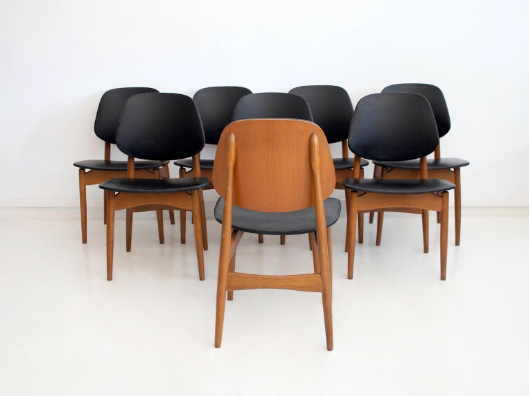 Set of eight wooden dining chairs with black synthetic leather seat and back. Slightly curved and tilted back which makes the chair comfortable to sit on. Good overall vintage condition.