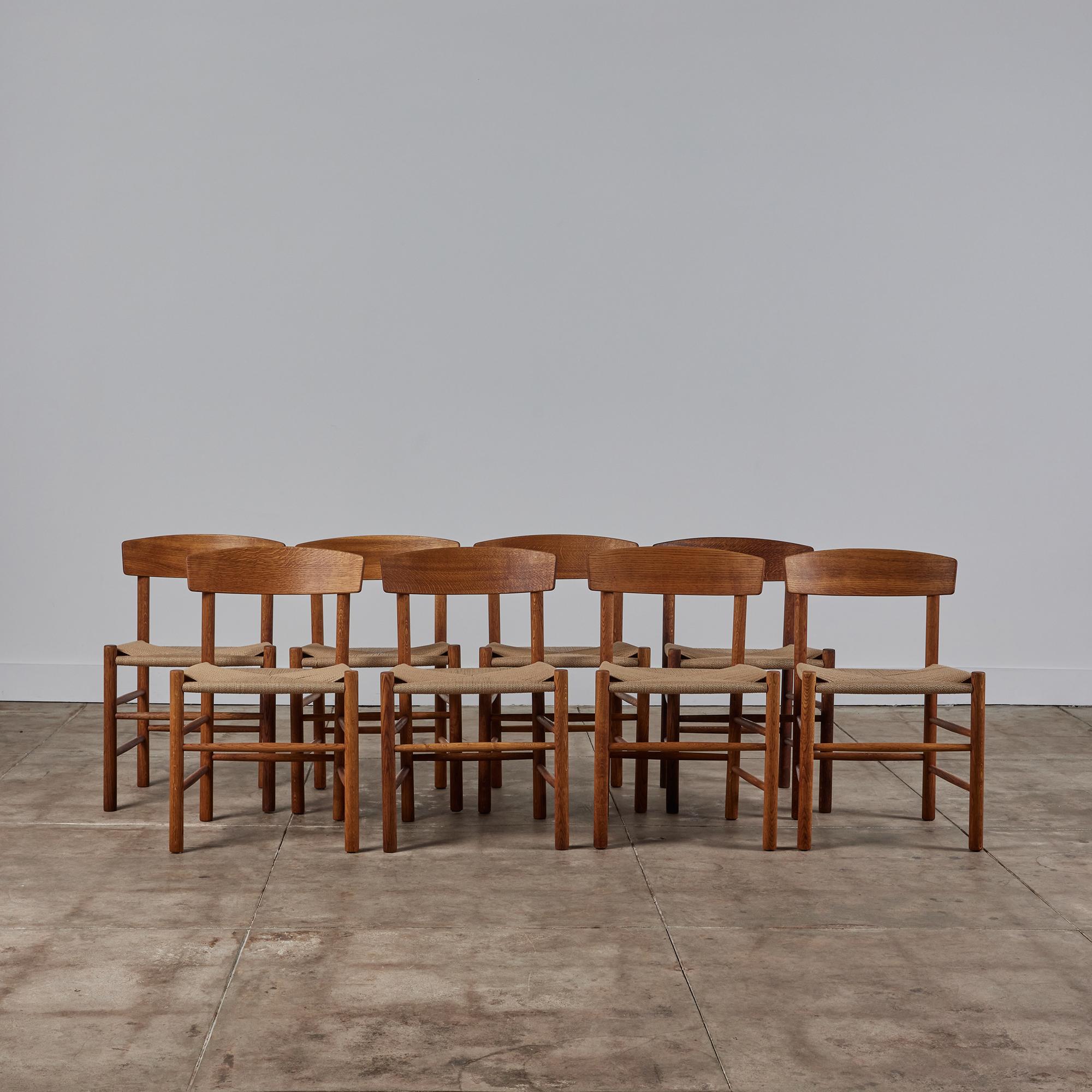 Set of eight dining chairs by Børge Mogensen for FDB Møbler beginning in 1947. The J39 or “People’s Chair,” has a frame of oak dowels, with a wide, curved backrest and a woven seat in Danish paper cord. Contrasting wooden plugs cover the hardware