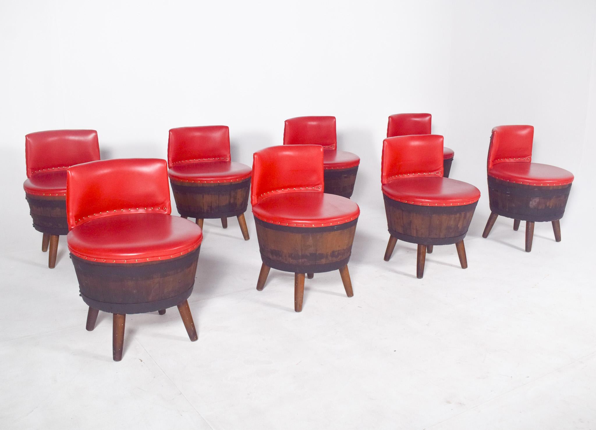 Eight benches made of wooden barrels. Each bench has a curved wooden base, sourced from darkened oak barrels, with a metal rim and varnished finish, preserving the rustic character and natural texture of the material. The seats are circular,