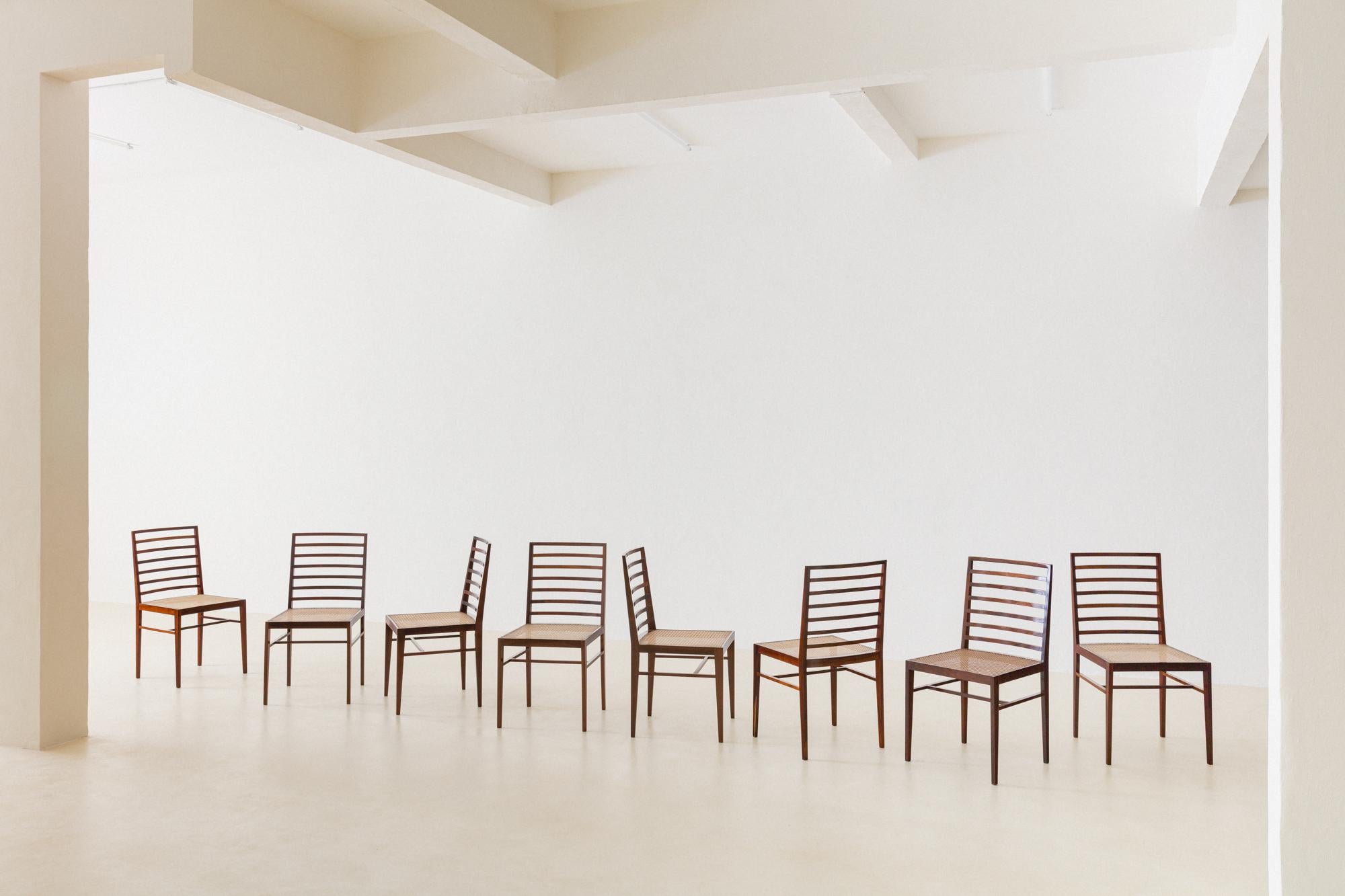 Dieses Set aus acht Stühlen wurde in den 1950er Jahren von Joaquim Tenreiro (1906-1992) entworfen. Diese atemberaubenden Stühle sind aus massivem Palisanderholz gefertigt und haben eine Rückenlehne mit Lattenrost und eine Sitzfläche aus
