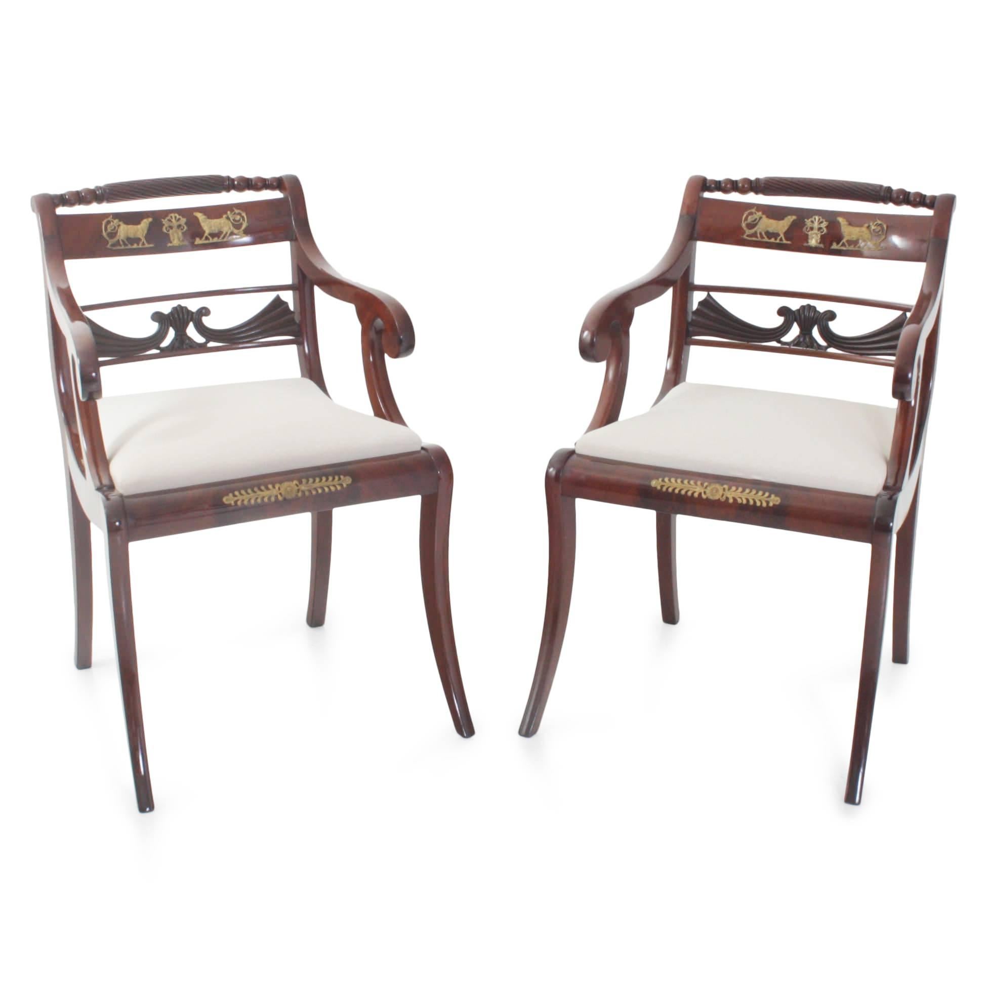 Set of eight chairs, consisting of six chairs and two armchairs out of mahogany. The chairs stand on sabre legs and are decorated with bronze fittings in the shape of lambs and leaves. The backrests show a pierced carved center strut in the shape of