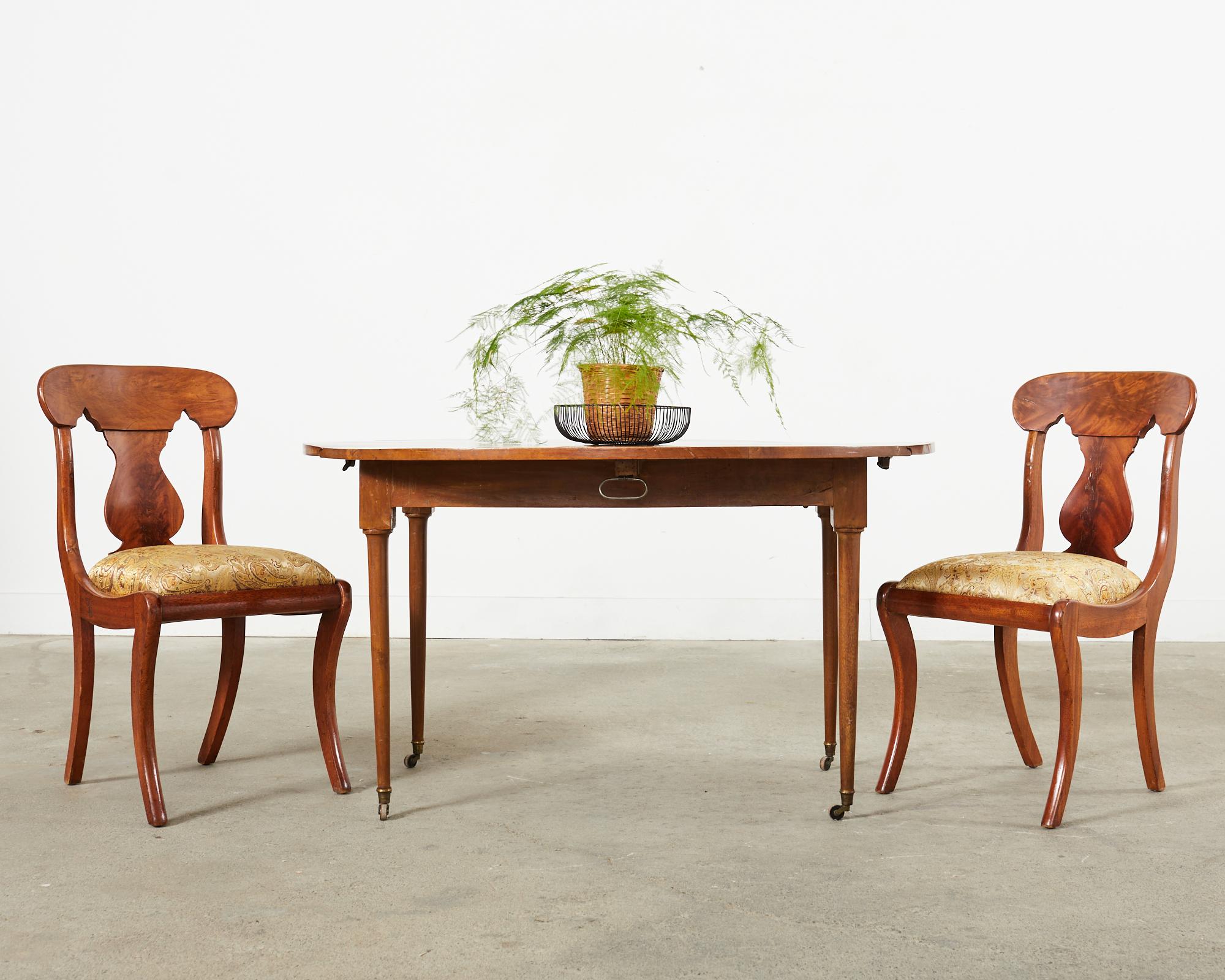 Distinctive set of eight French dining chairs crafted from radiant flame mahogany veneers. The chairs are made in the Empire revival style with a gracefully curved vasiform shaped back splat. The seat is supported by klismos style saber legs for a