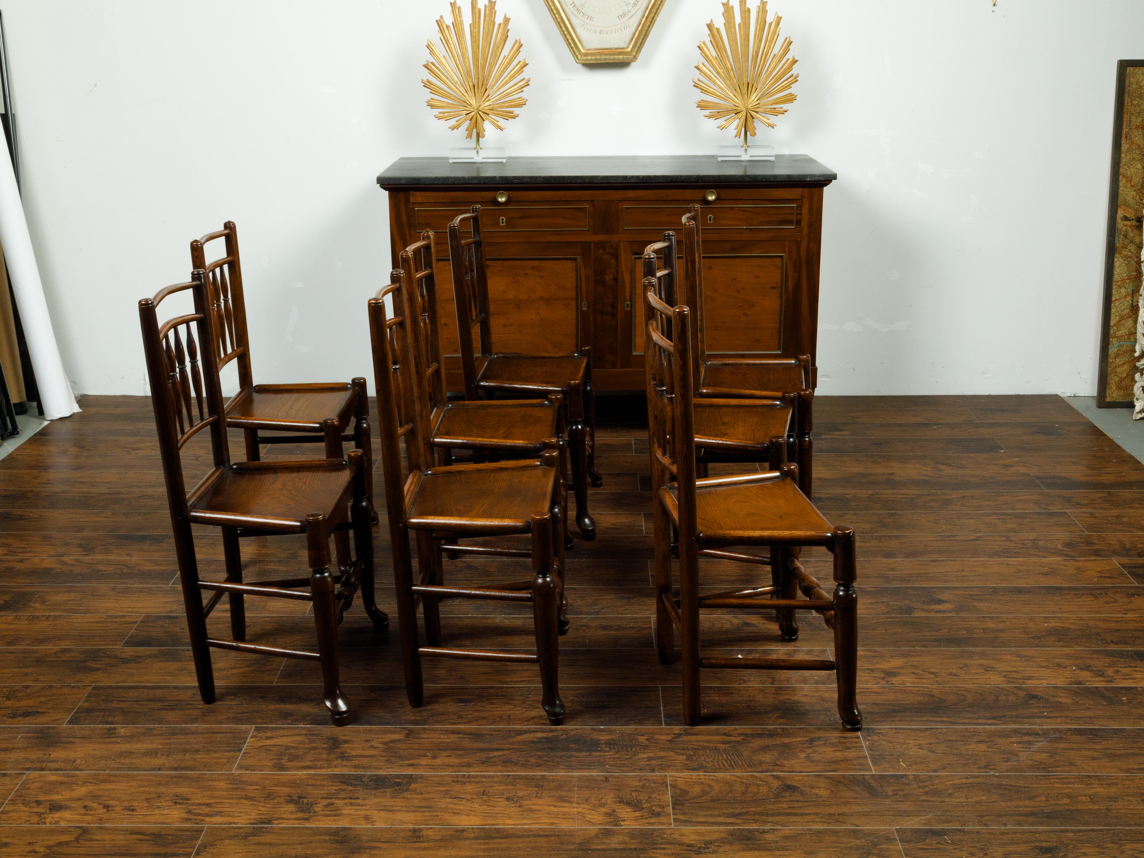 An English set of eight oak dining room side chairs from the late 19th century, with spindle motifs and wooden seats. Created in England during the last quarter of the 19th century, each of this set of eight dining room chairs features a spindle