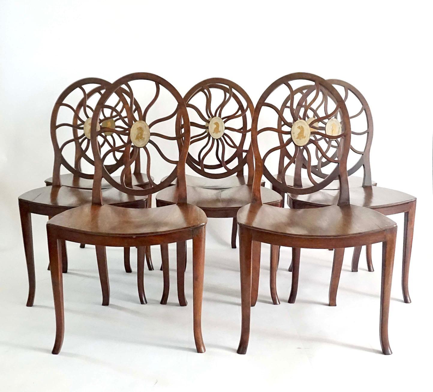 Rare and elegant set of eight circa 1790 English George III period Hepplewhite style hall or dining chairs of solid mahogany construction having oval backs with radiating 'cobweb' or 'spider web' variant design splats with central oval reserves