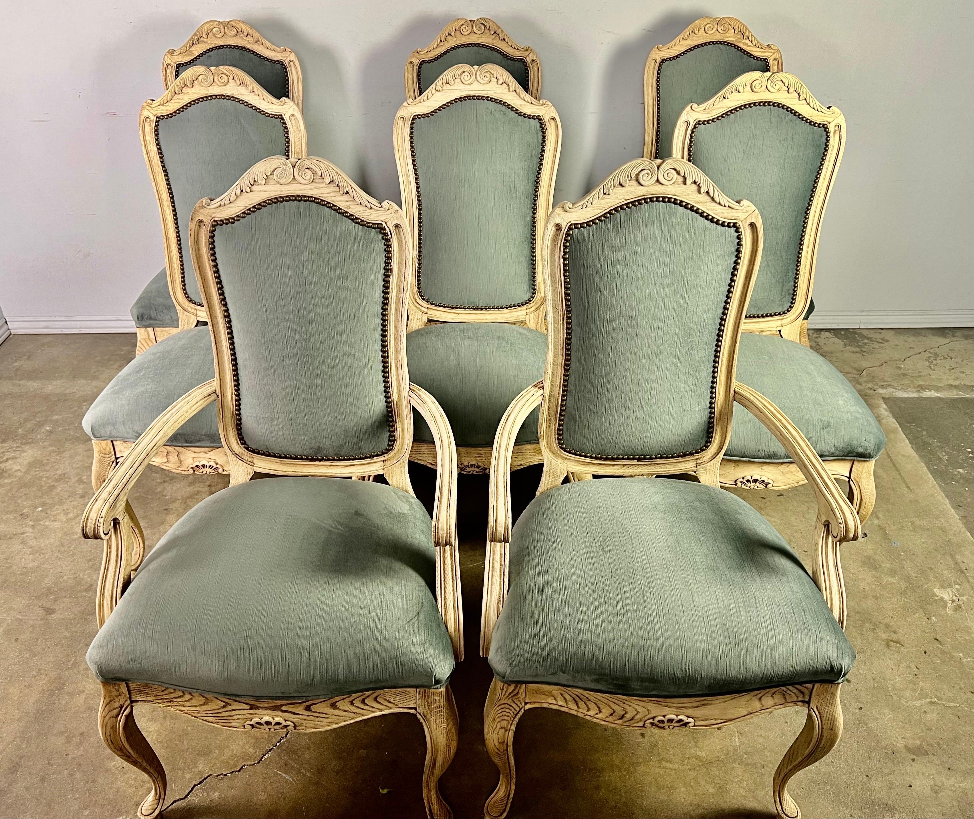 Set of eight painted French Louis XV style dining chairs newly upholstered in blue velvet and finished with a row of nailheads. The chairs stand on cabriole legs that end in rams head feet. There are an opposing pair of acanthus leaves depicted at